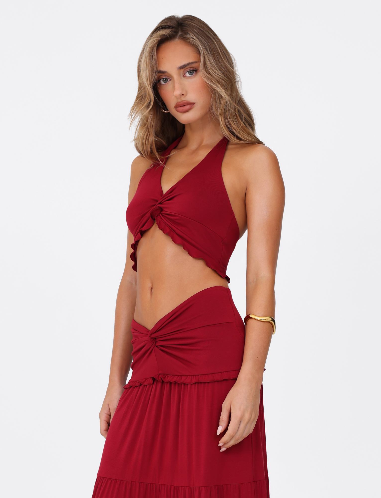 A woman with wavy light brown hair wears the TIGERMIST KATYA HALTER TOP in red, styled with a matching skirt featuring knotted details. She stands against a plain white background, looking at the camera with a neutral expression.