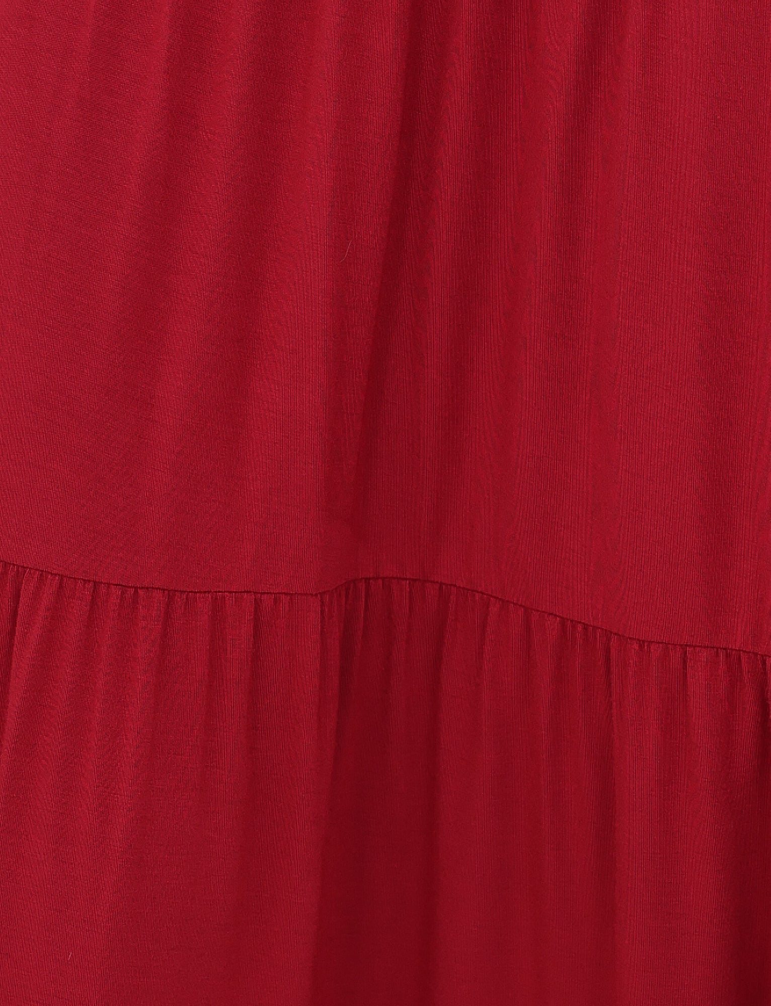The KATYA MAXI SKIRT by TIGERMIST features a close-up of red gathered pleats creating soft, flowing folds. The high-stretch fabric offers a smooth appearance with a slight shine, suggesting a gentle, relaxed drape.