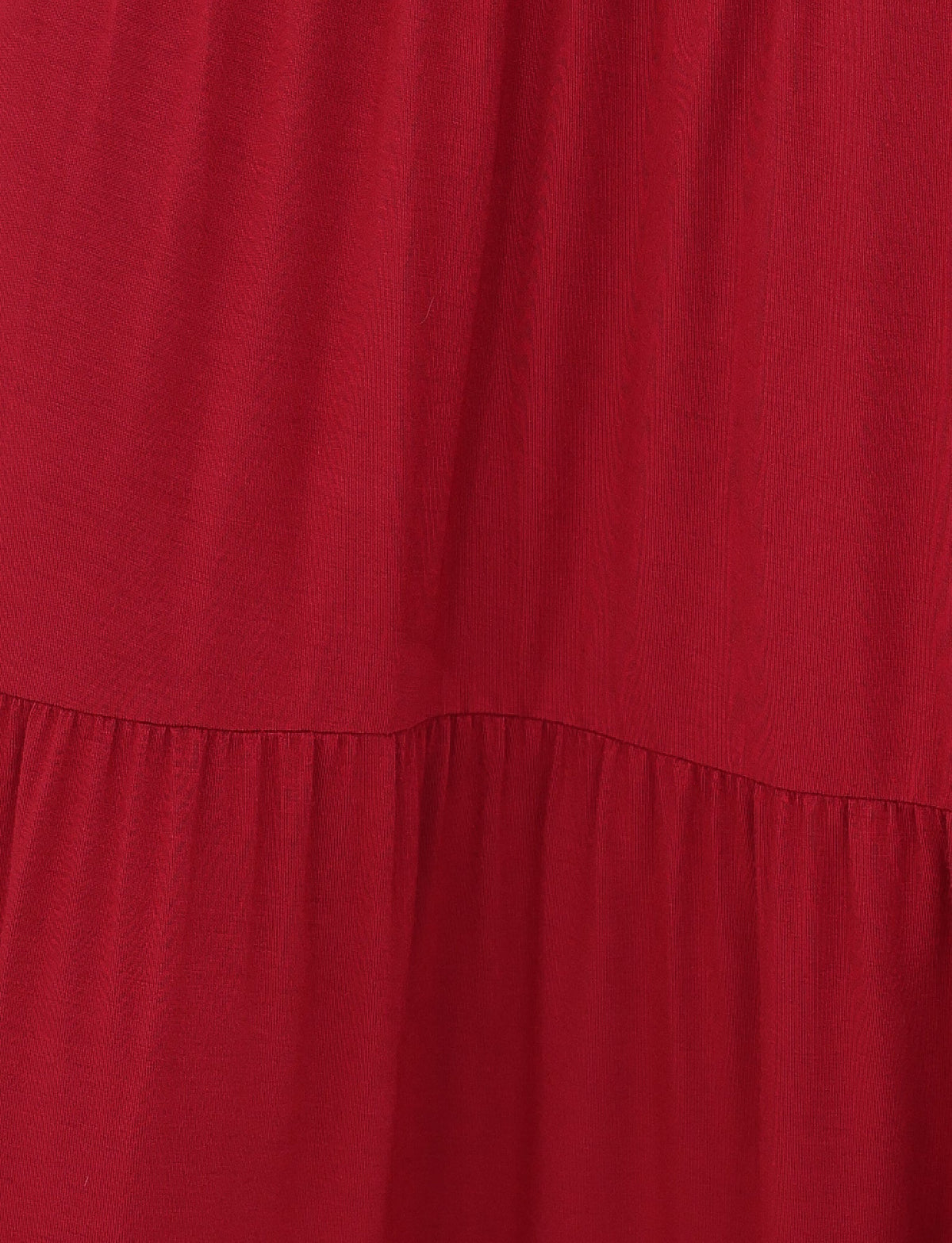 The KATYA MAXI SKIRT by TIGERMIST features a close-up of red gathered pleats creating soft, flowing folds. The high-stretch fabric offers a smooth appearance with a slight shine, suggesting a gentle, relaxed drape.