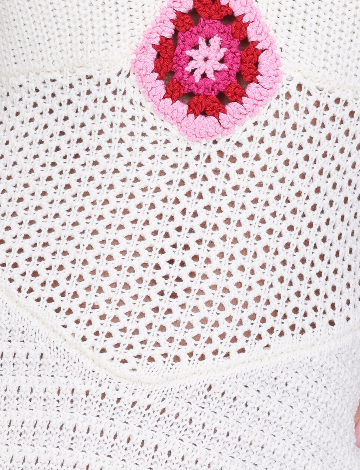 Close-up of the TENZIN MINI DRESS - CREAM by TIGERMIST, featuring airy white crochet fabric and a standout pink and red granny square patch near the top.