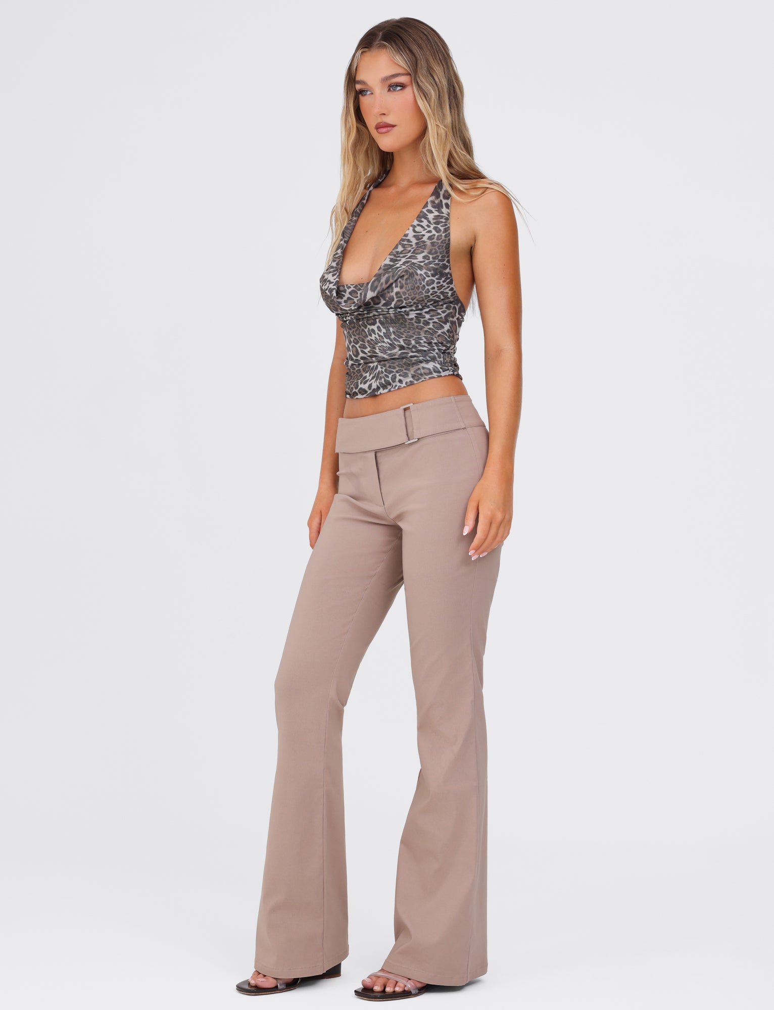 A woman with long hair is wearing a sleeveless, patterned top with a plunging neckline and the VESPER PANT - BROWN : TAN from TIGERMIST. She is standing against a plain white background, facing slightly to the right. She is also wearing open-toed black shoes that complement her fitted silhouette.