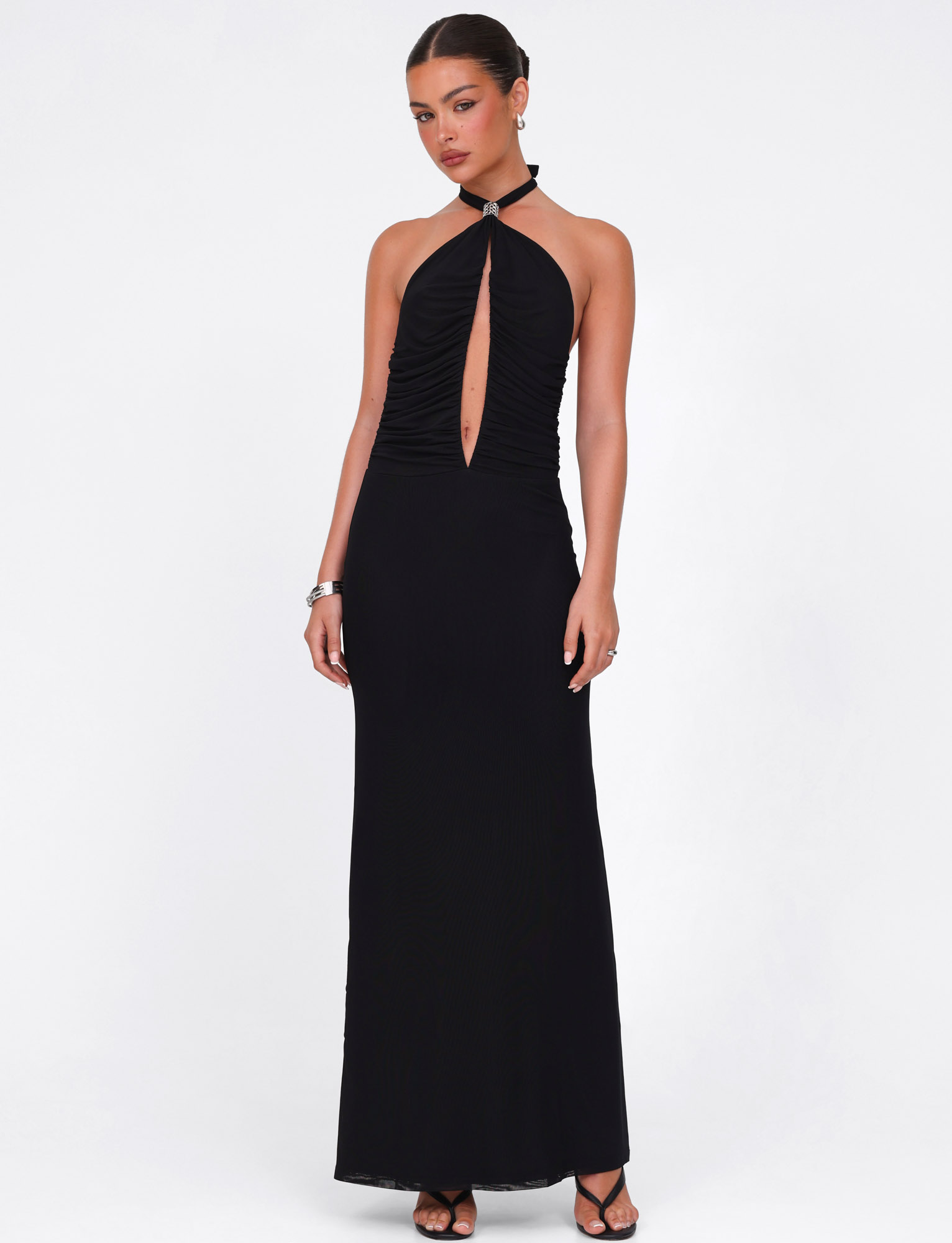 A woman models the TIGERMIST ZARA MAXI DRESS in black, featuring a halter neckline and front keyhole cutout. The high-stretch fabric accentuates her silhouette, styled simply against a white background with pulled-back hair, bracelets, and earrings.
