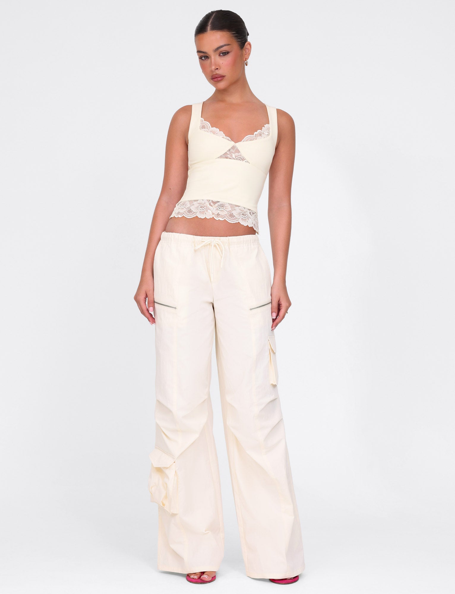 A person is wearing the Dione Lace Top in soft butter yellow by TIGERMIST, paired with high-waisted wide-leg pants featuring a drawstring. Their hair is styled up, echoing a sleek buttery finish, as they stand against a plain white background with relaxed arms.