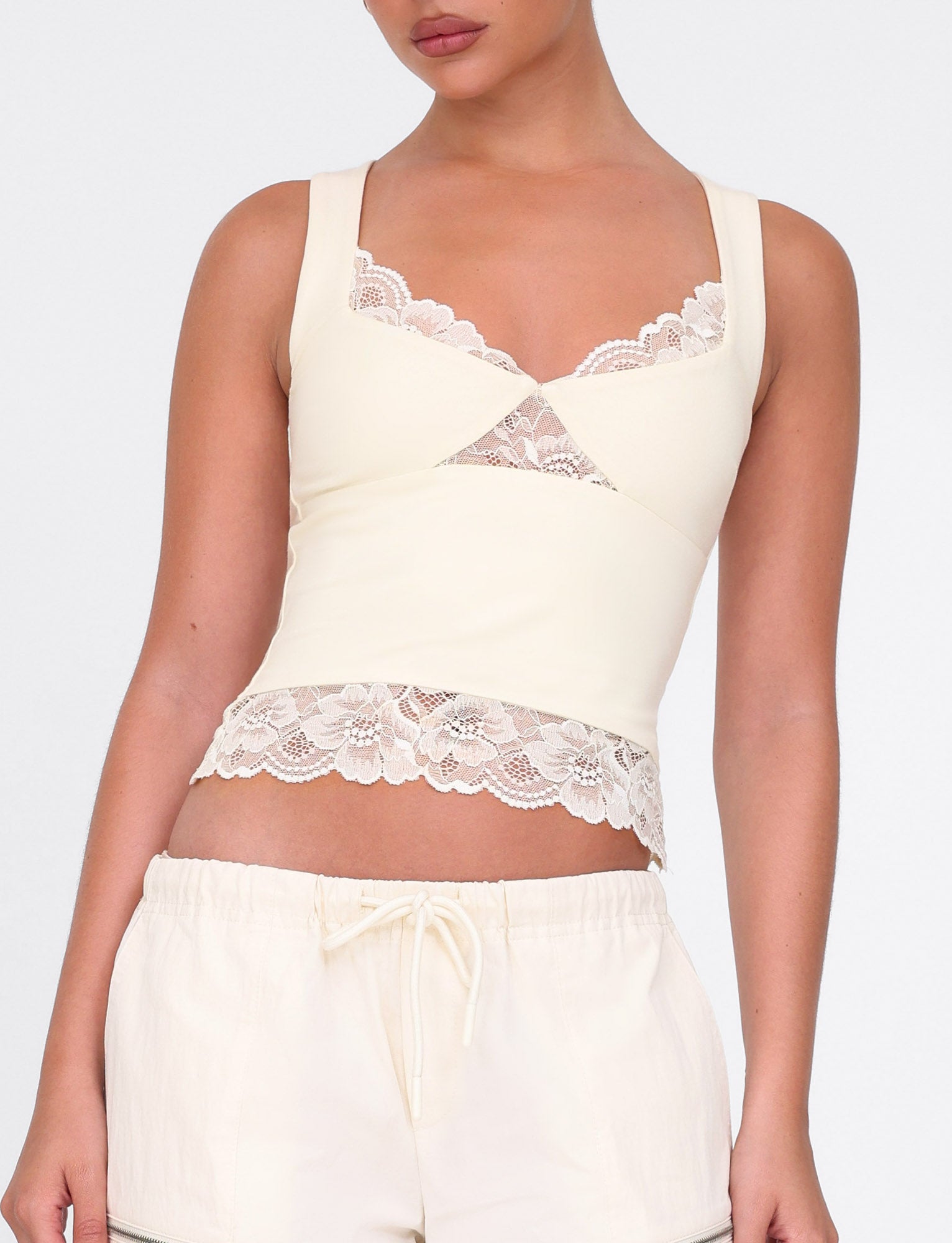 A person is wearing the DIONE LACE TOP by TIGERMIST in soft butter, paired with buttery jersey drawstring shorts, against a plain white background.