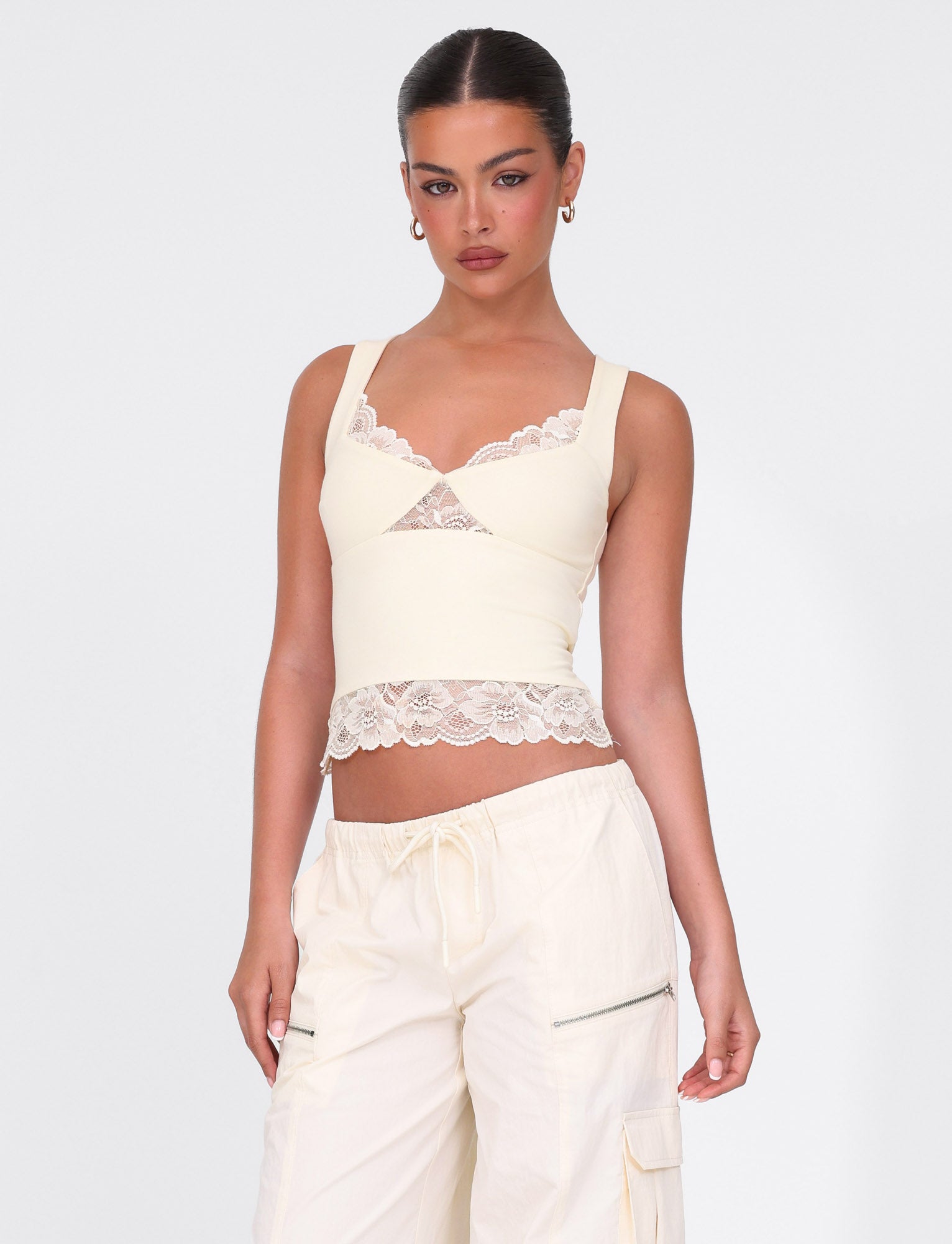 A person stands confidently against a plain background, wearing the TIGERMIST DIONE LACE TOP in Soft Butter and matching cargo pants. Their dark hair is pulled back neatly.