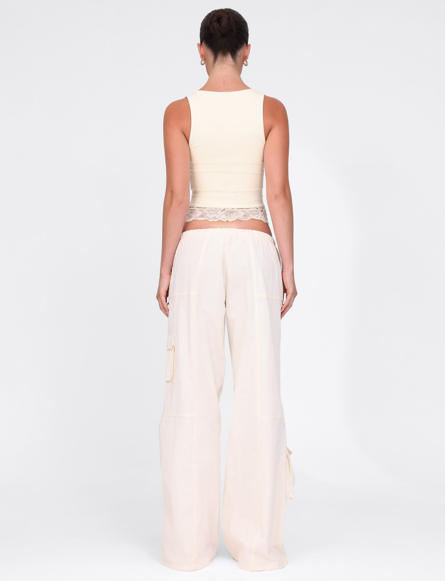 A person stands facing away, wearing a sleeveless beige crop top and TIGERMIST HERMIONE PANT in Soft Butter yellow. Their hair is up against a plain white background.