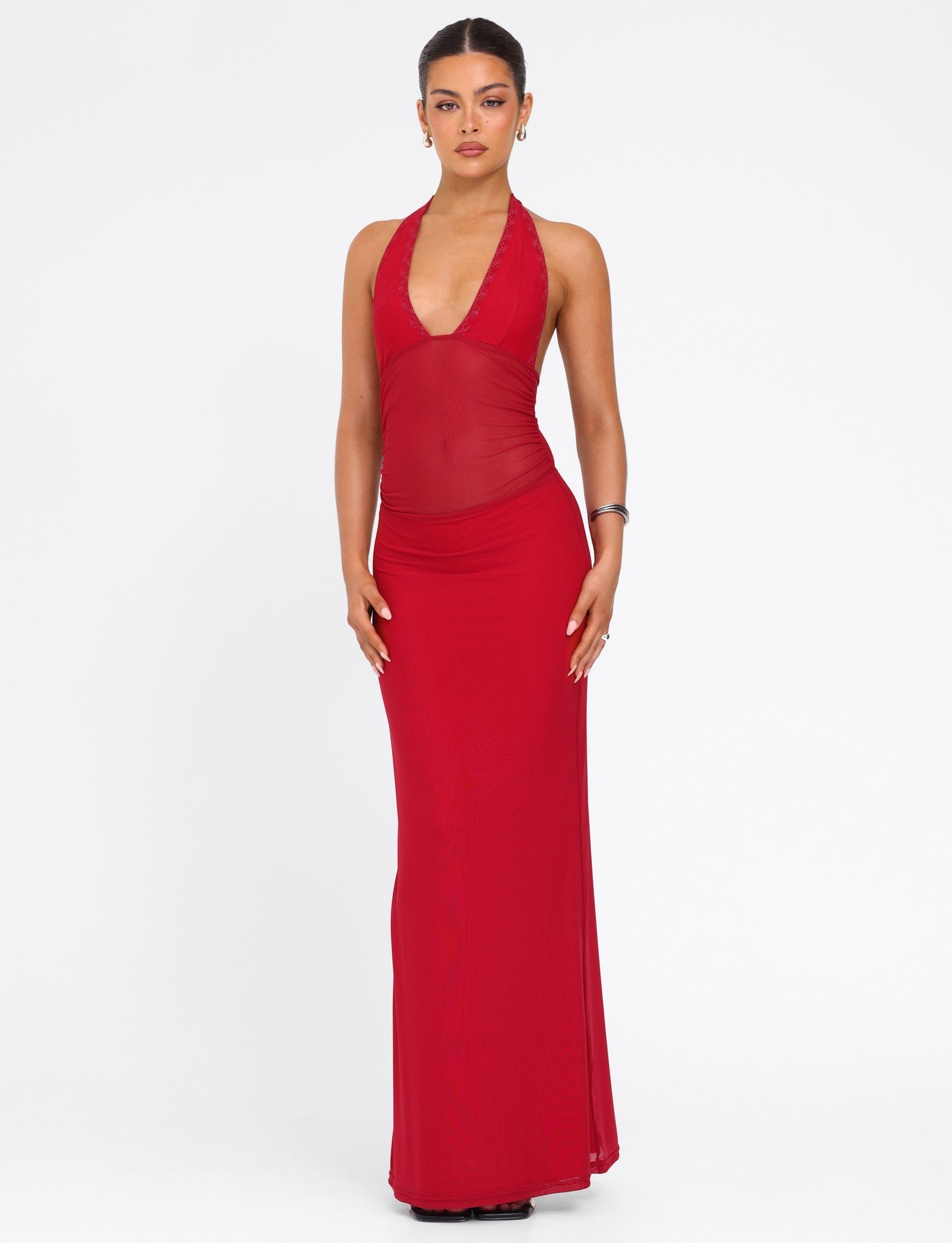A woman stands against a white background wearing the TIGERMIST BRESILY MAXI DRESS in red, a sleeveless, form-fitting halter dress with a deep V-neckline. Her hair is pulled back and she wears minimal jewelry.