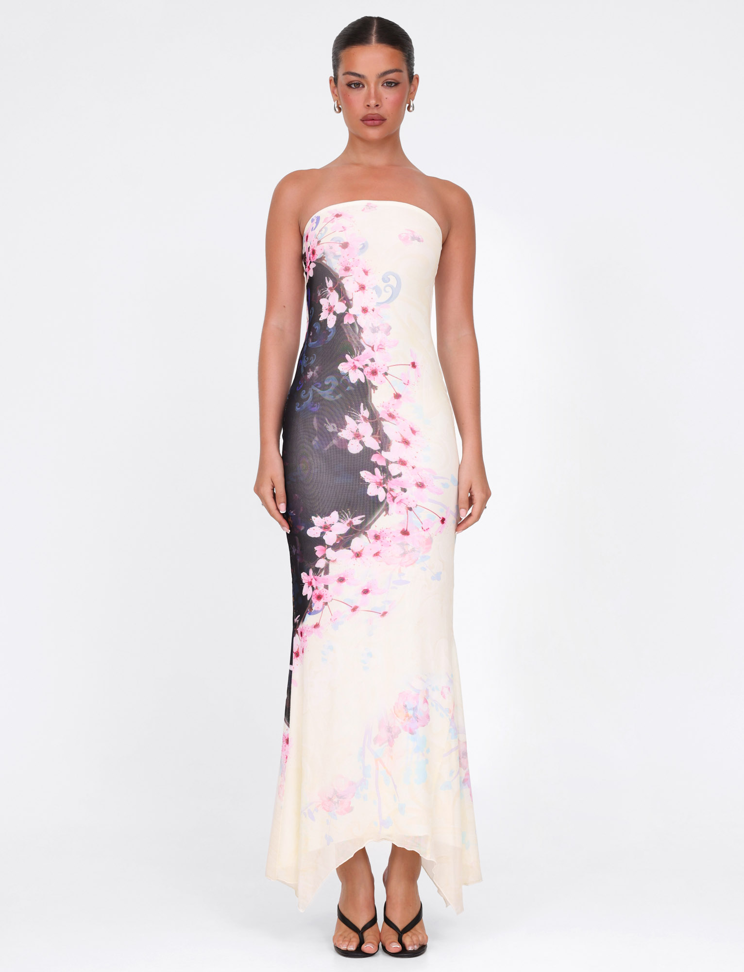 A woman faces forward in the TIGERMIST LILLIAN MAXI DRESS - MULTI: FLORAL: CHERRY BLOSSUM, her hair tied back and wearing black sandals, set against a plain white background.