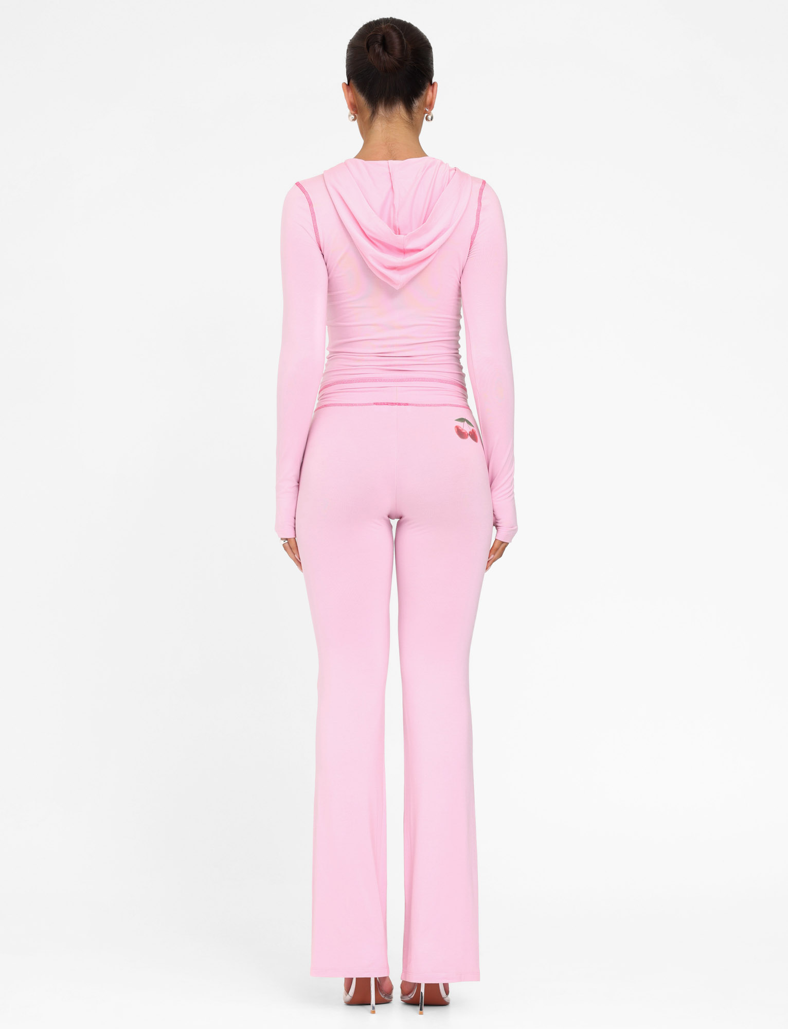 A woman, facing away from the camera, wears TIGERMIST’s BLAYZE PANT in soft pink with a matching light pink fitted hooded top against a plain white background.