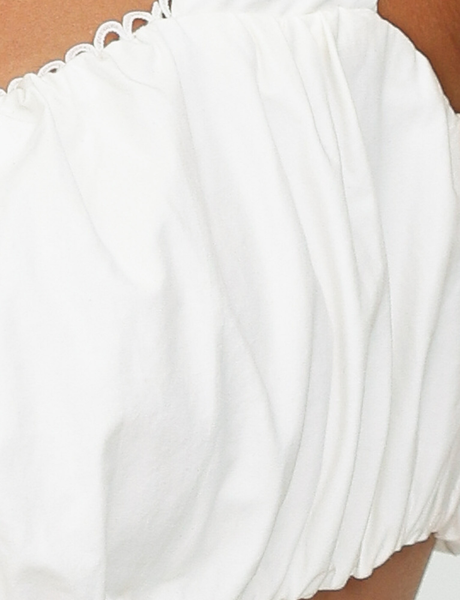 Close-up of a person wearing the TIGERMIST SABRA TOP in white, an off-the-shoulder cropped top with ruched fabric. Background and other details are not visible.