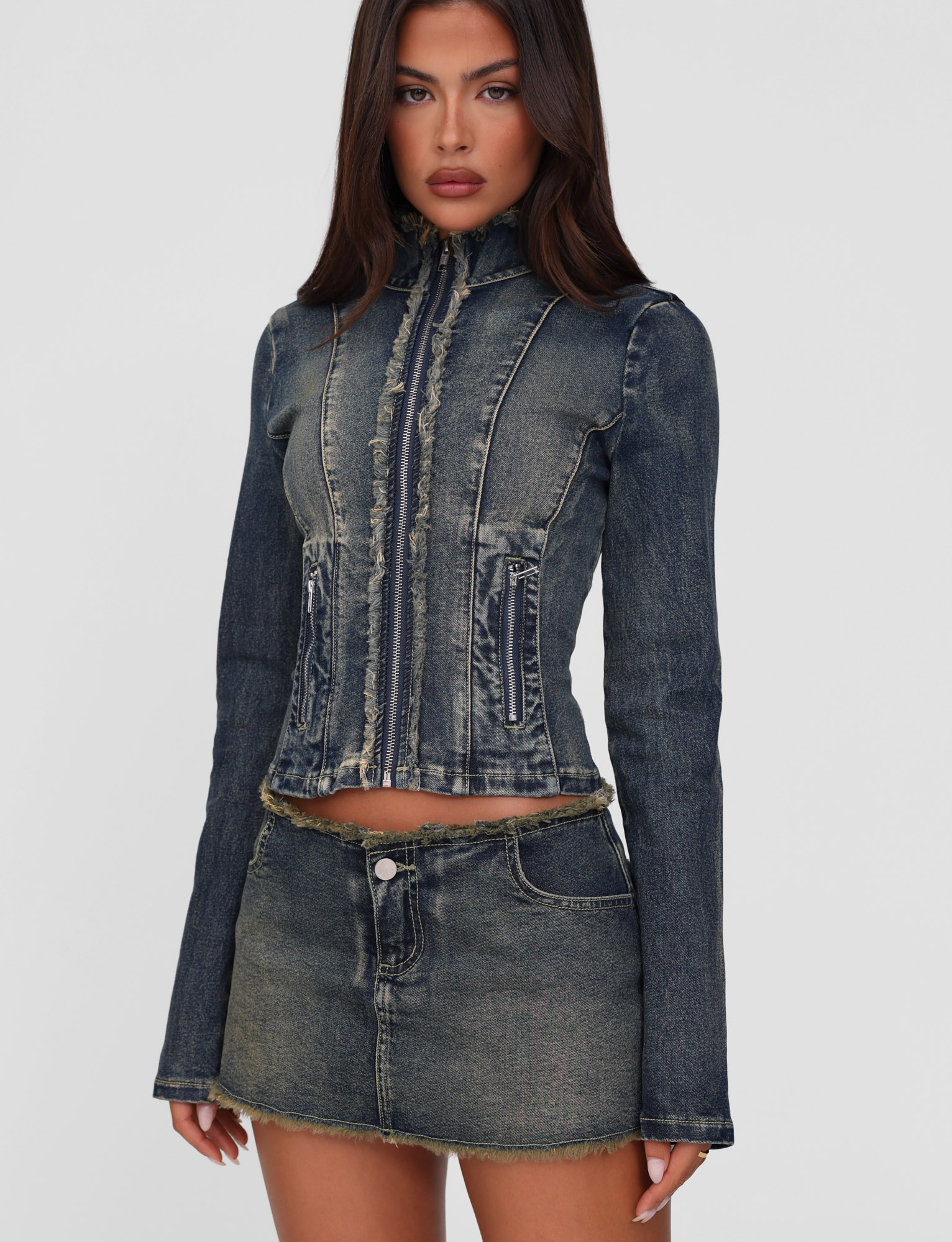 A woman wearing the TIGERMIST OPHELIE JACKET in denim blue with frayed edges and a matching mini skirt, standing against a plain white background.