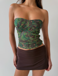 A woman wearing the TIGERMIST DULCE CORSET - GREEN : CAMO stands against a plain white background, paired with a brown mini skirt. Her face is not visible in the image.