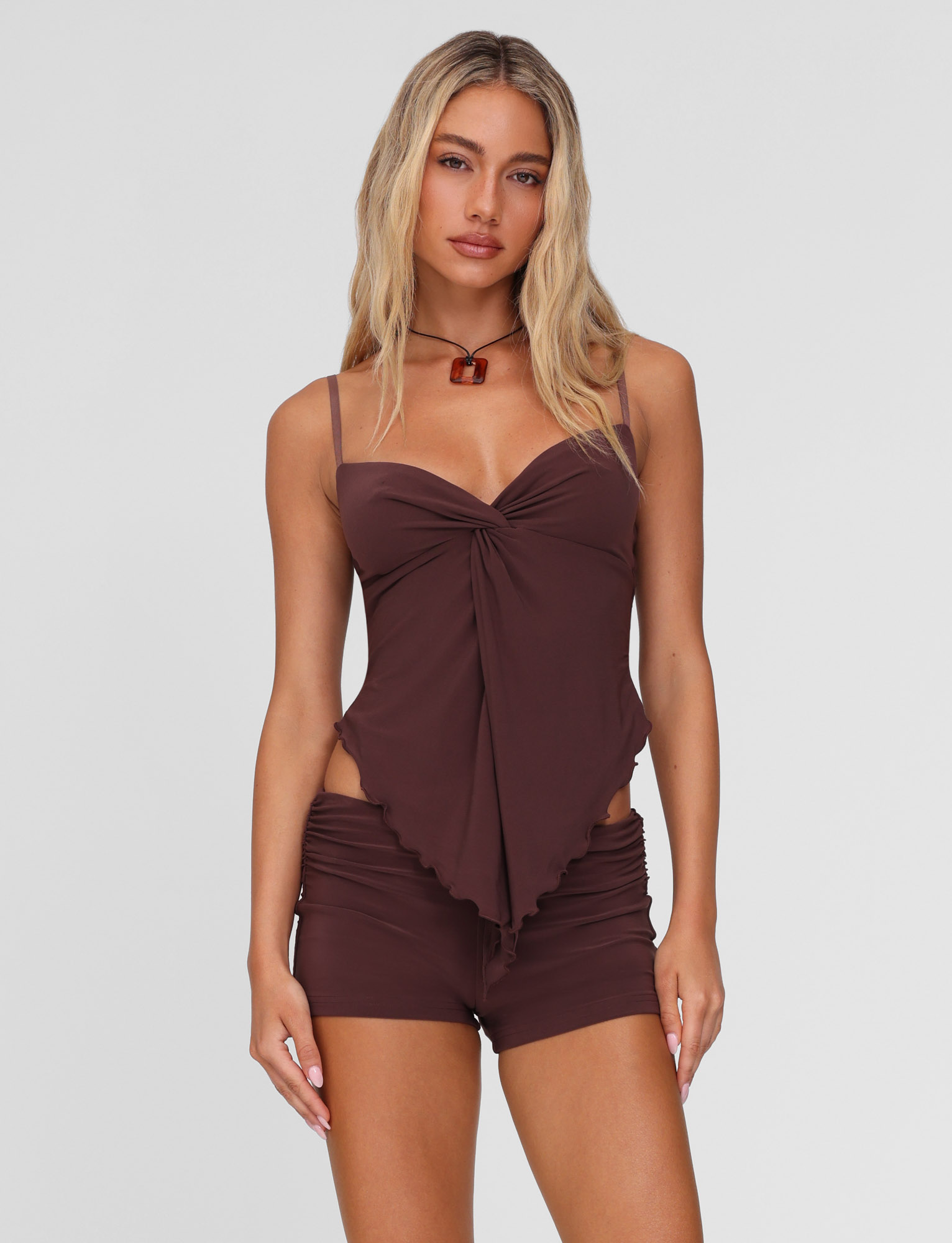 A woman with long blonde hair wears the TIGERMIST JOVIENNE SHORT - BROWN: CHOCOLATE, paired with a matching sleeveless chocolate brown top and choker, posing against a plain light background with a neutral expression.
