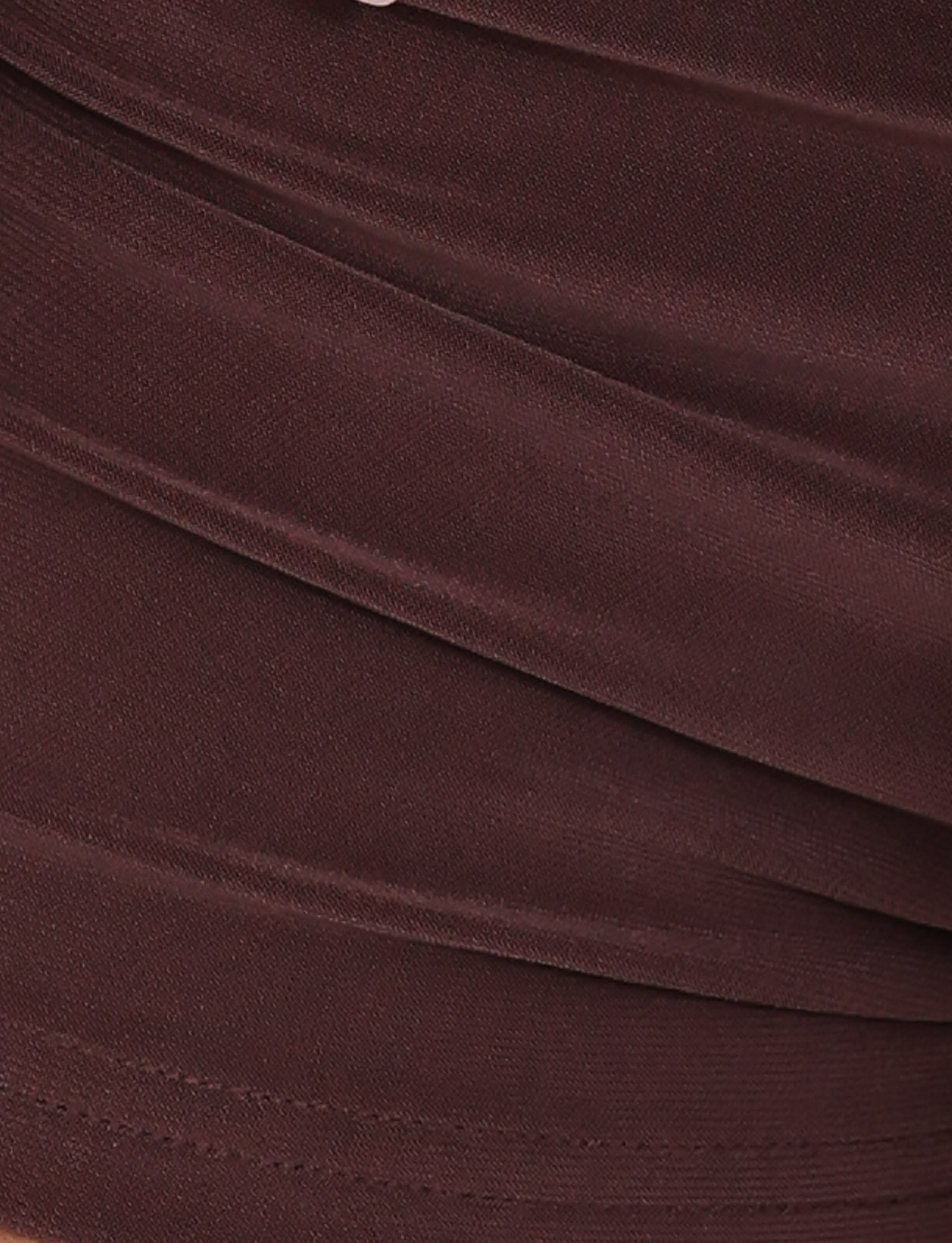 Close-up of overlapping, ruched fabric reveals the smooth, slightly shiny texture of TIGERMIST's JOVIENNE SHORT - BROWN : CHOCOLATE, with soft shadows and diagonal lines evoking an elegantly modern chocolate brown jersey finish.