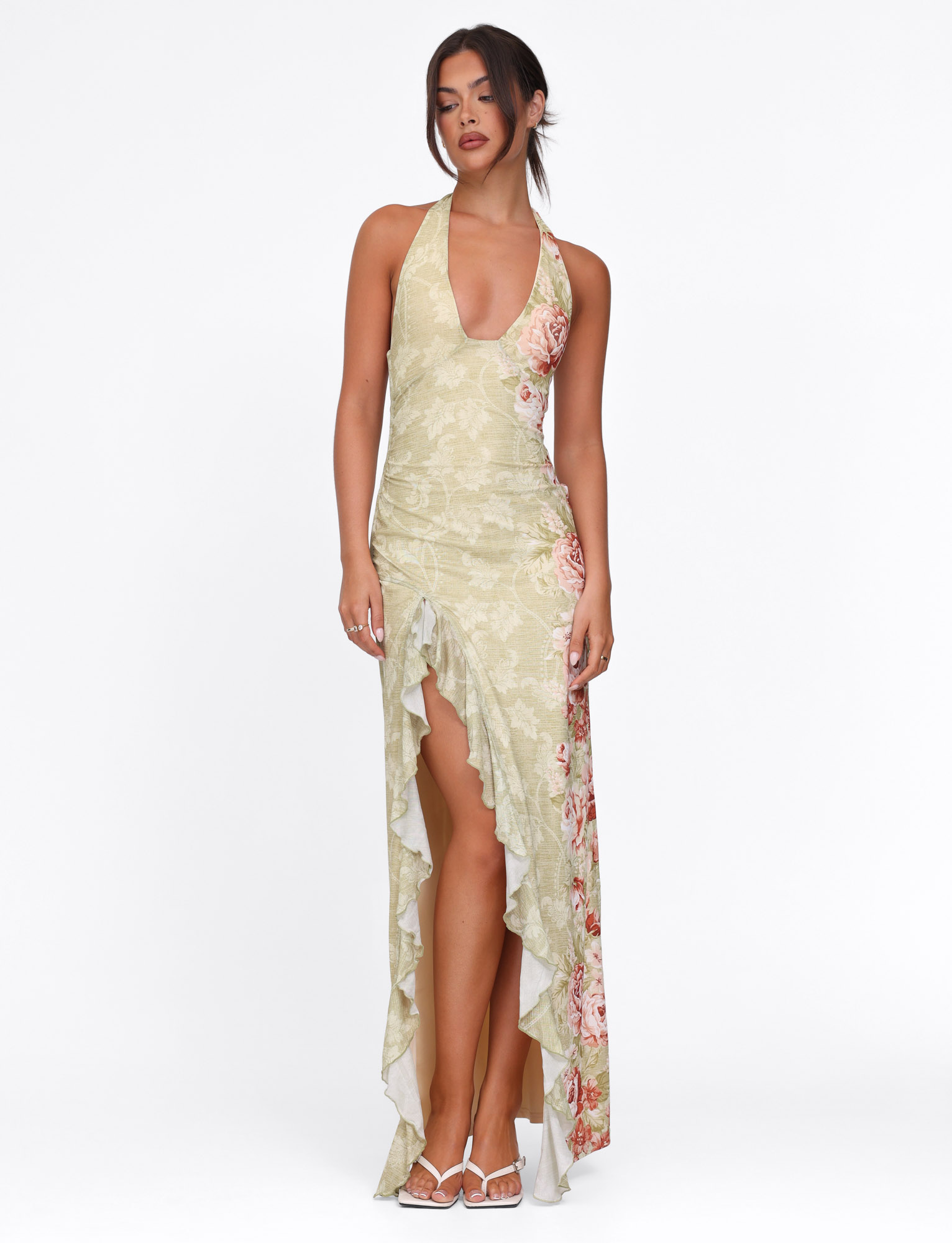 A woman models the TIGERMIST SIRENA MAXI DRESS in yellow floral rose stripe, featuring a halter neck, deep neckline, and high-low ruffled hem, standing against a plain white background with her hands by her sides.