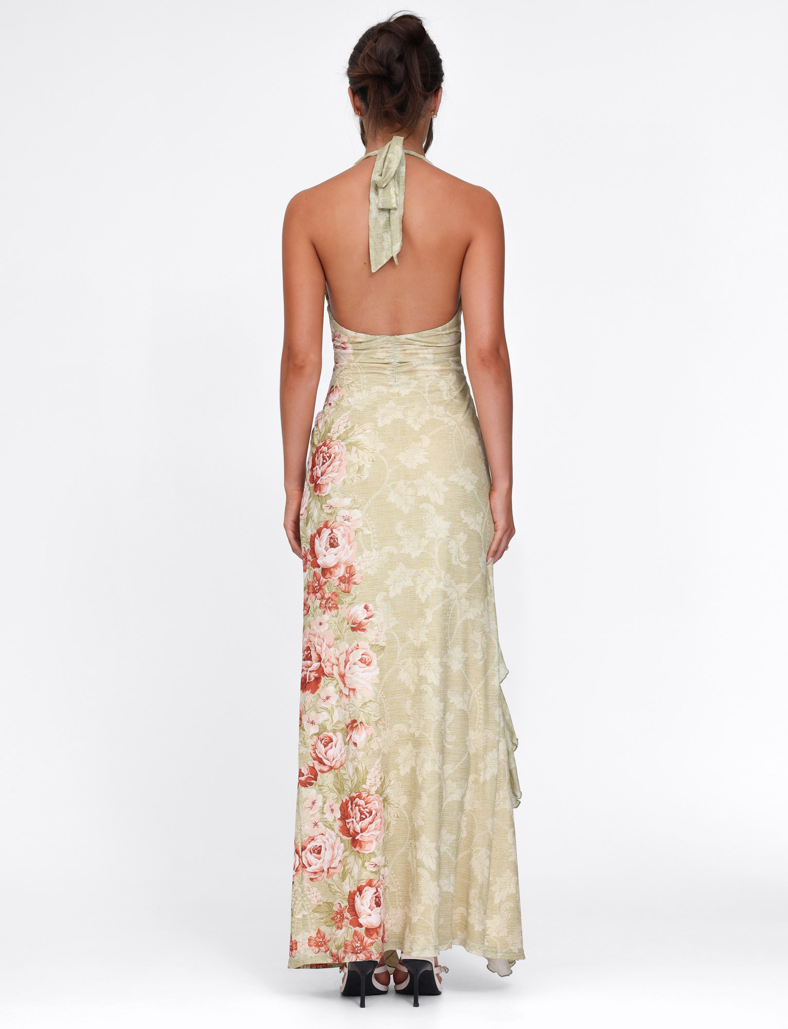 A woman with brown hair in a loose updo wears the TIGERMIST SIRENA MAXI DRESS - YELLOW, featuring a rose stripe floral print, halter neck, open back, and black heels.