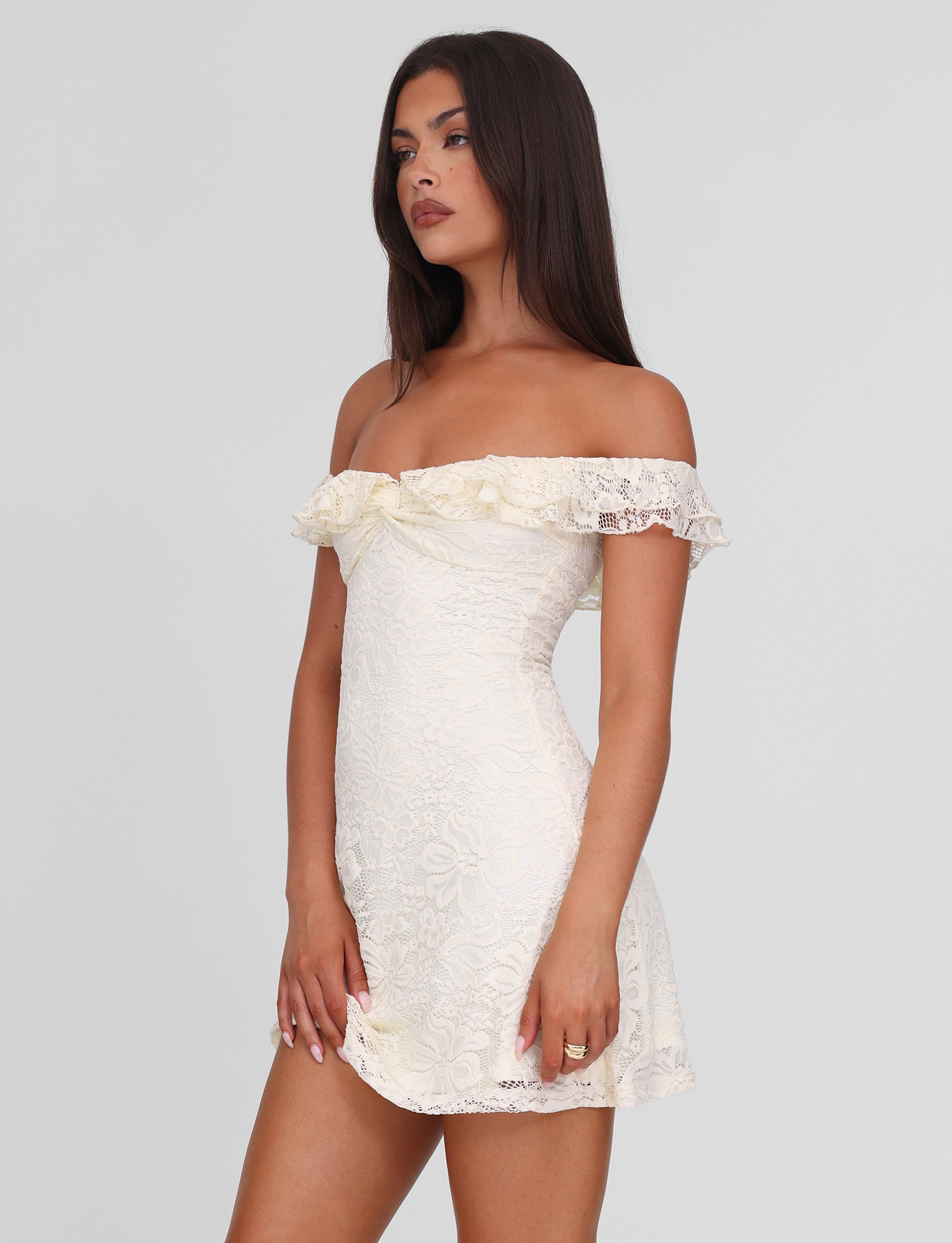 A woman with long dark hair wears the TIGERMIST DENALI LACE MINI DRESS in cream lace. Posed against a plain light background, she looks to the side with a neutral expression.