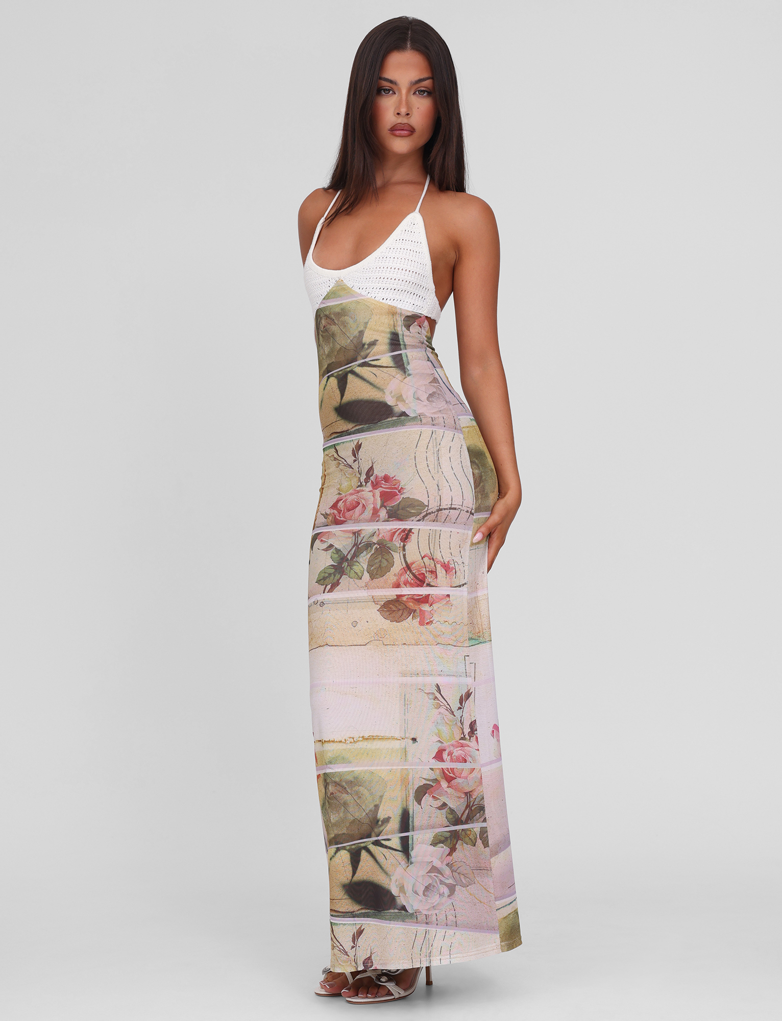 A woman with long dark hair models the TIGERMIST TILLEY MAXI DRESS - ROSE POSTCARD, featuring contrast crochet bust cups and an exclusive print skirt, as she stands confidently against a white background.