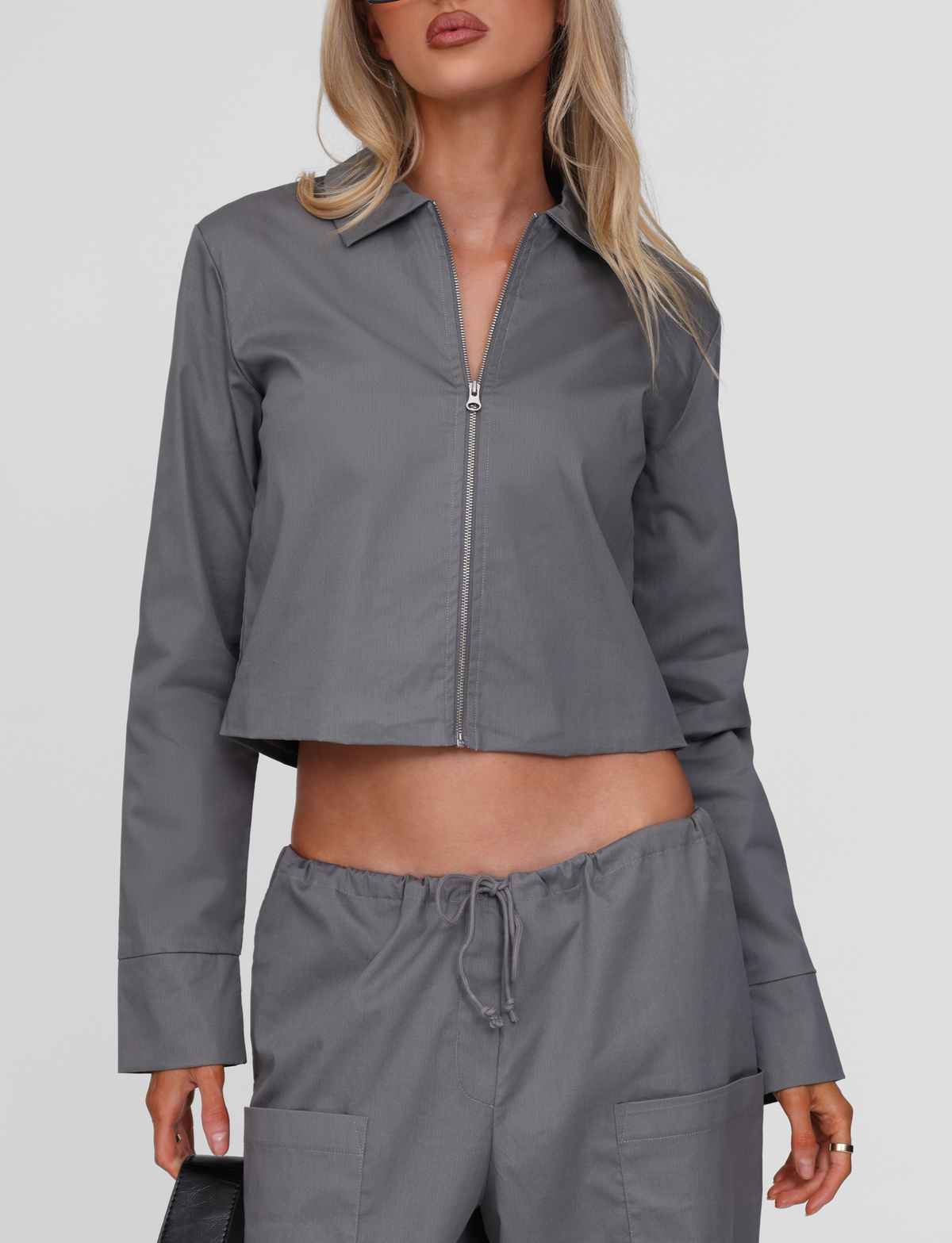 A woman with long blonde hair models the TIGERMIST TYSHA JACKET - CHARCOAL, a boxy-fit cargo jacket with matching drawstring pants in lightly ribbed fabric, standing against a plain white background. Her face is partially visible.