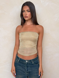 A woman with long straight brown hair wears the TIGERMIST HARRIETT TUBE TOP in gold and blue jeans, posing against a beige textured wall with a neutral expression.