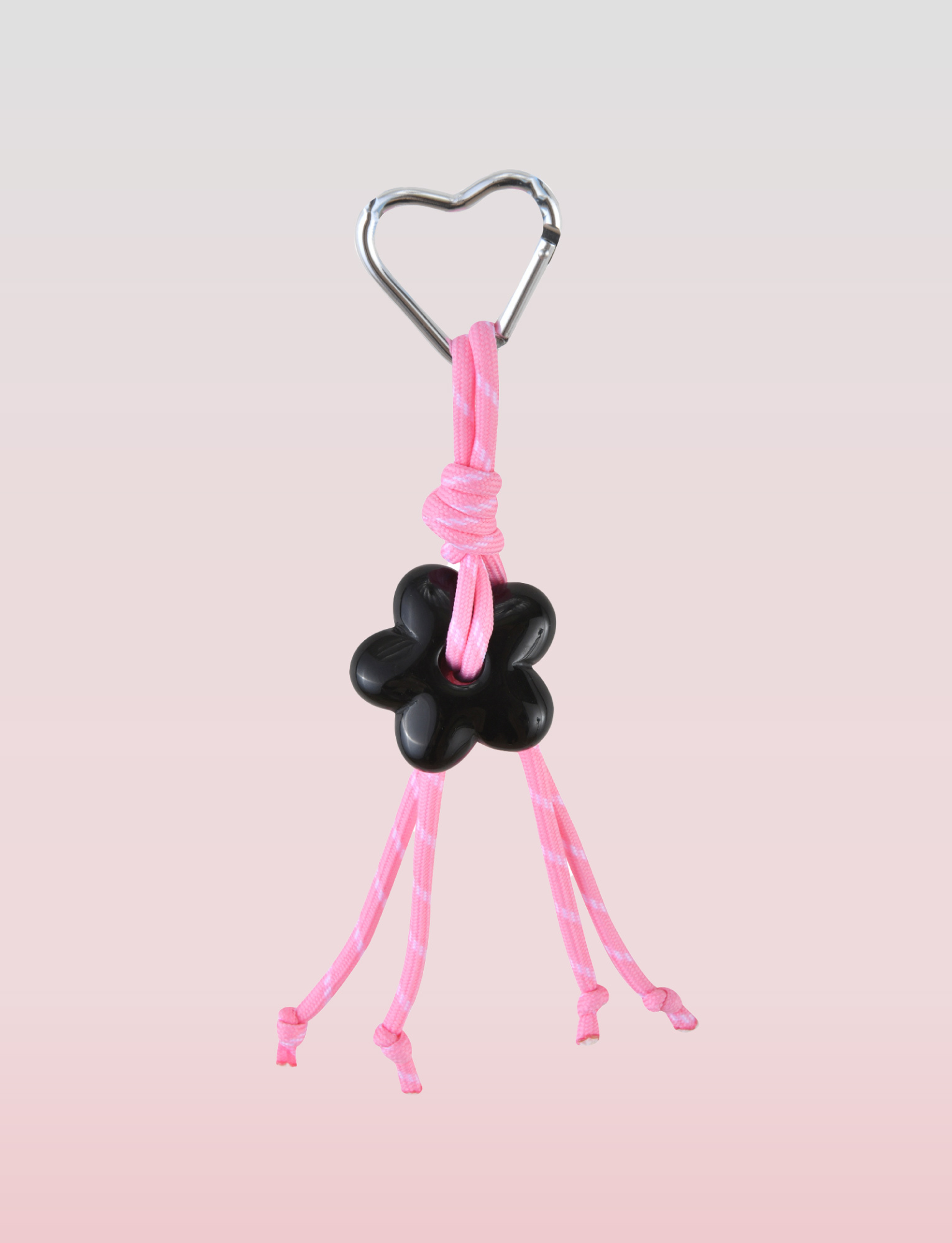 The TIGERMIST MIRIAM KEYCHAIN - HOT PINK features a metal heart clasp, pink cords with a black flower-shaped bead, and four loose ends, all set against a soft pink gradient—perfect as a stylish accessory.