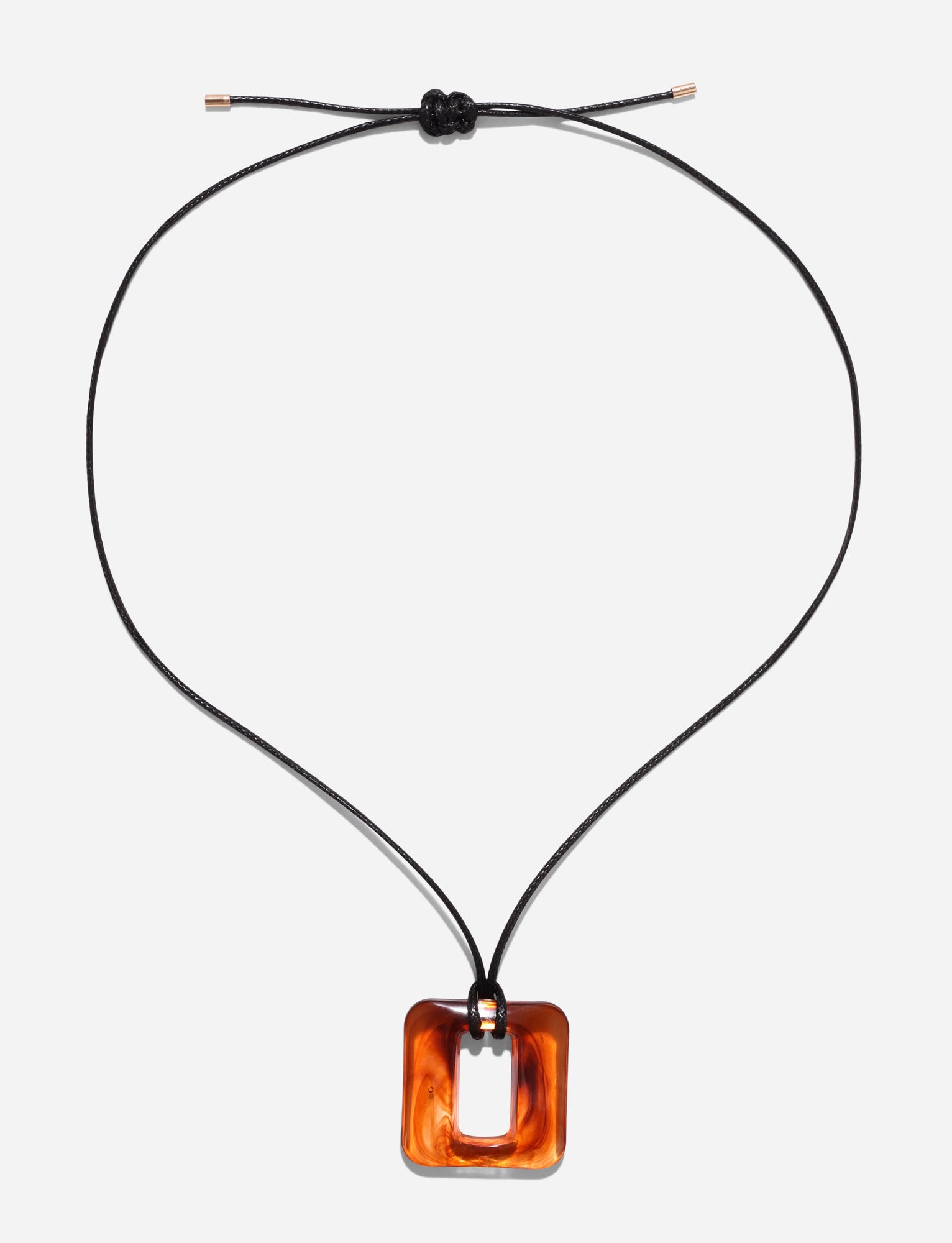 The TIGERMIST MIRREN SQUARE NECKLACE - BROWN features a black woven cord with a smooth, glossy, orange-brown square pendant with a central hole. It embraces minimalist design and is secured by a simple knot at the top.