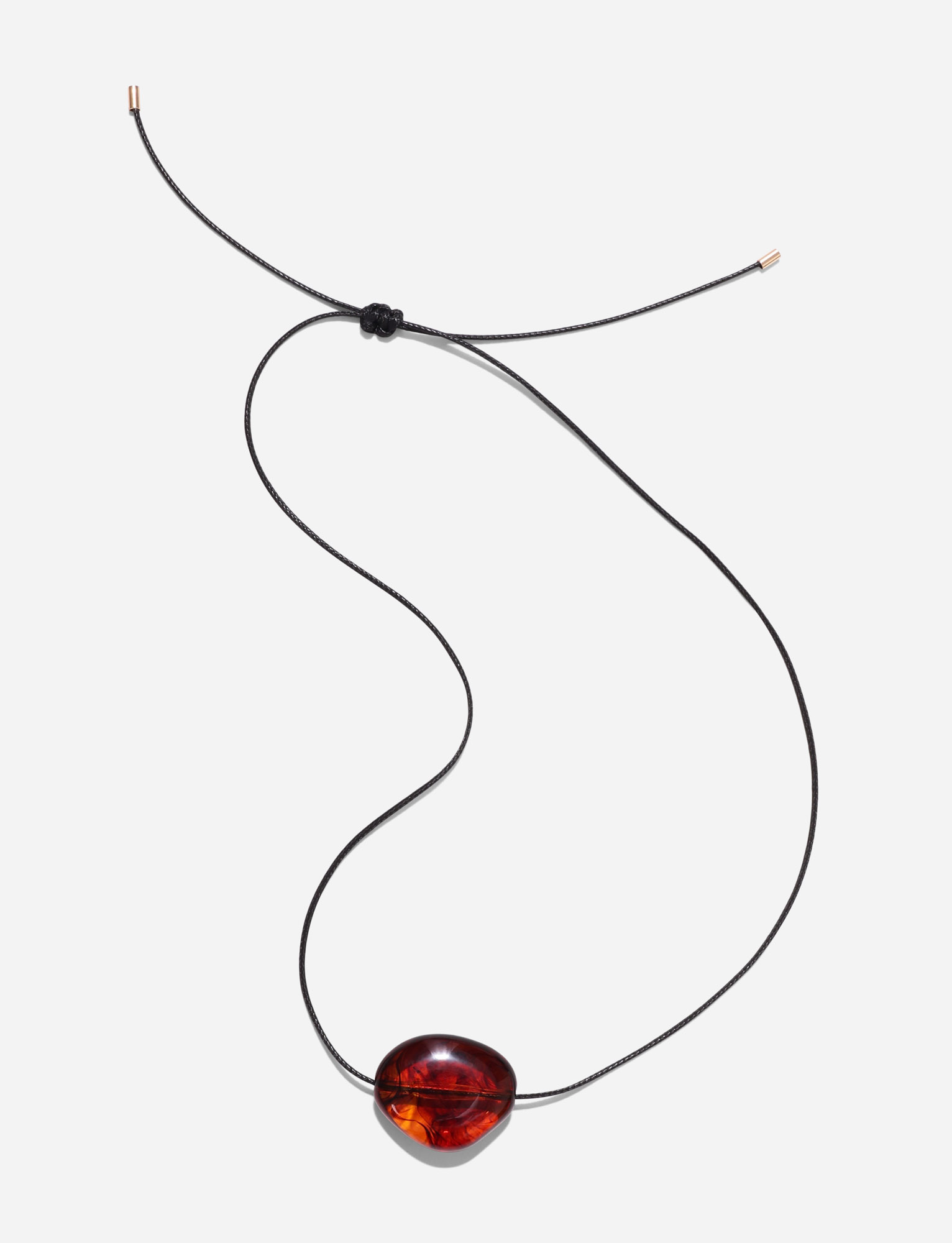 The TIGERMIST SOLENE NECKLACE - BROWN features a dark woven cord with a polished, oval amber pendant. Its minimalist design includes adjustable knots and metallic tips, shown on a plain white background.