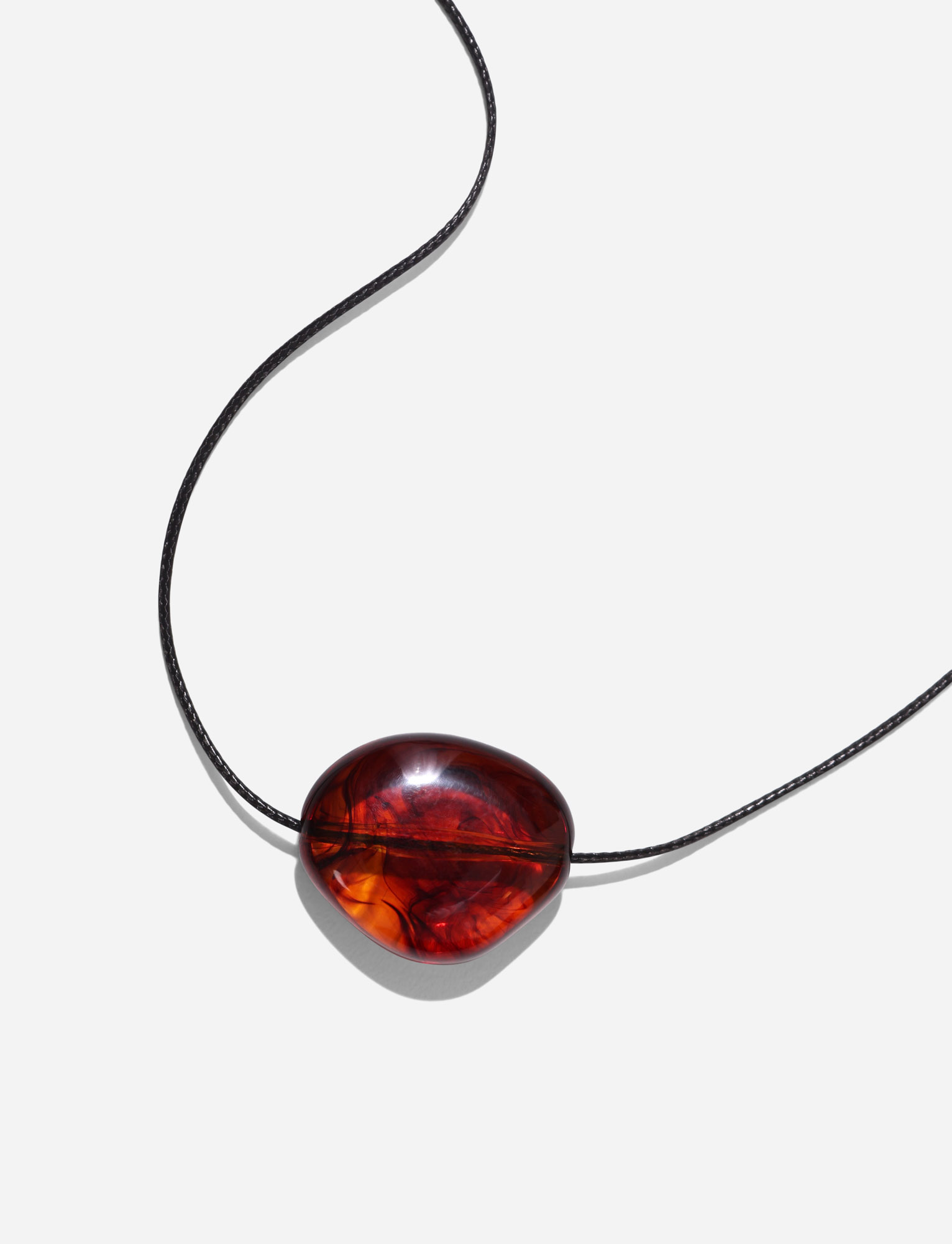 The SOLENE NECKLACE - BROWN by TIGERMIST features a polished, oval amber pendant with reddish-brown tones on a woven cord, set against a plain white background.
