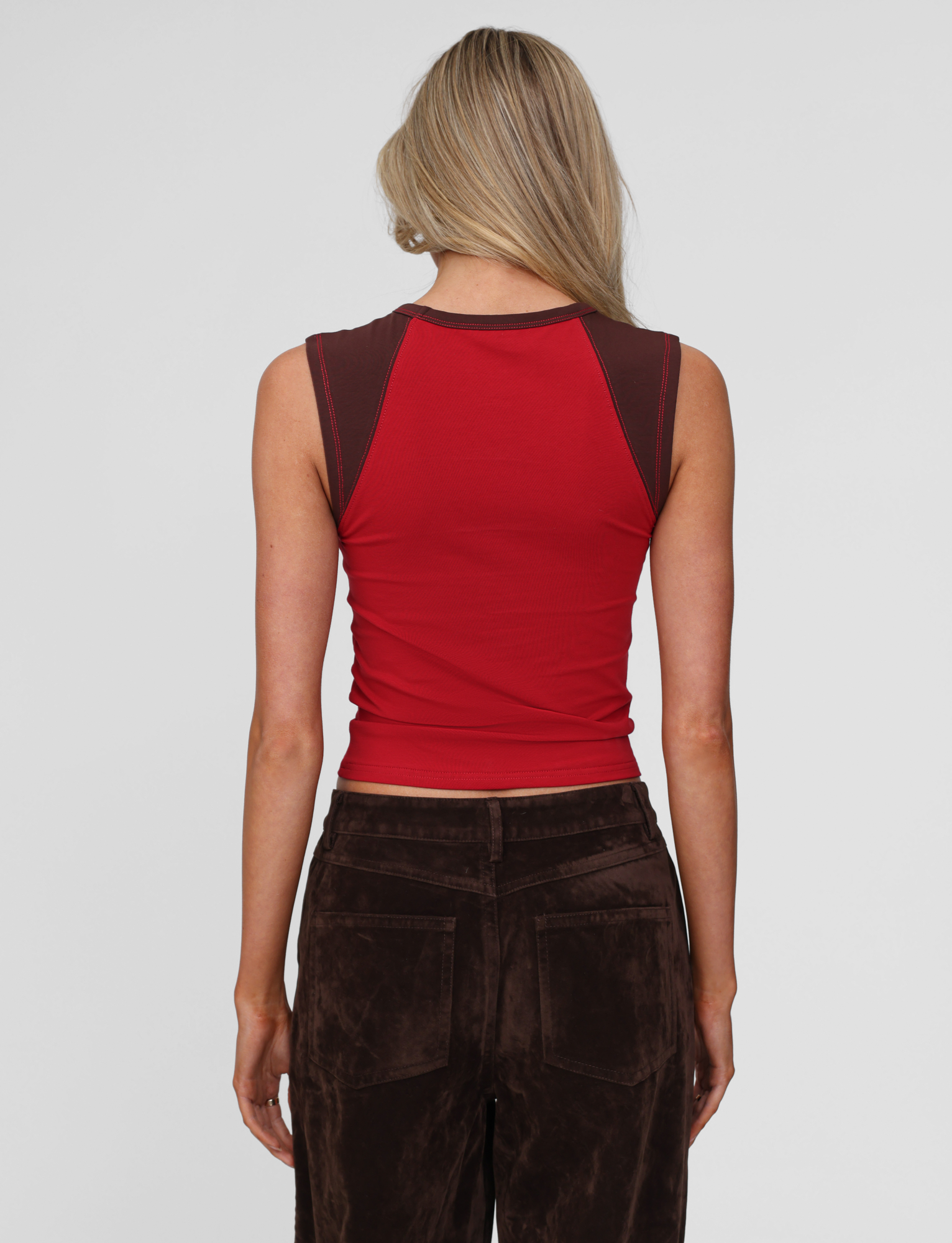 A woman with long blonde hair, seen from behind, wears the TIGERMIST FIERA TEE in red and brown velvet pants, posed against a plain light background.