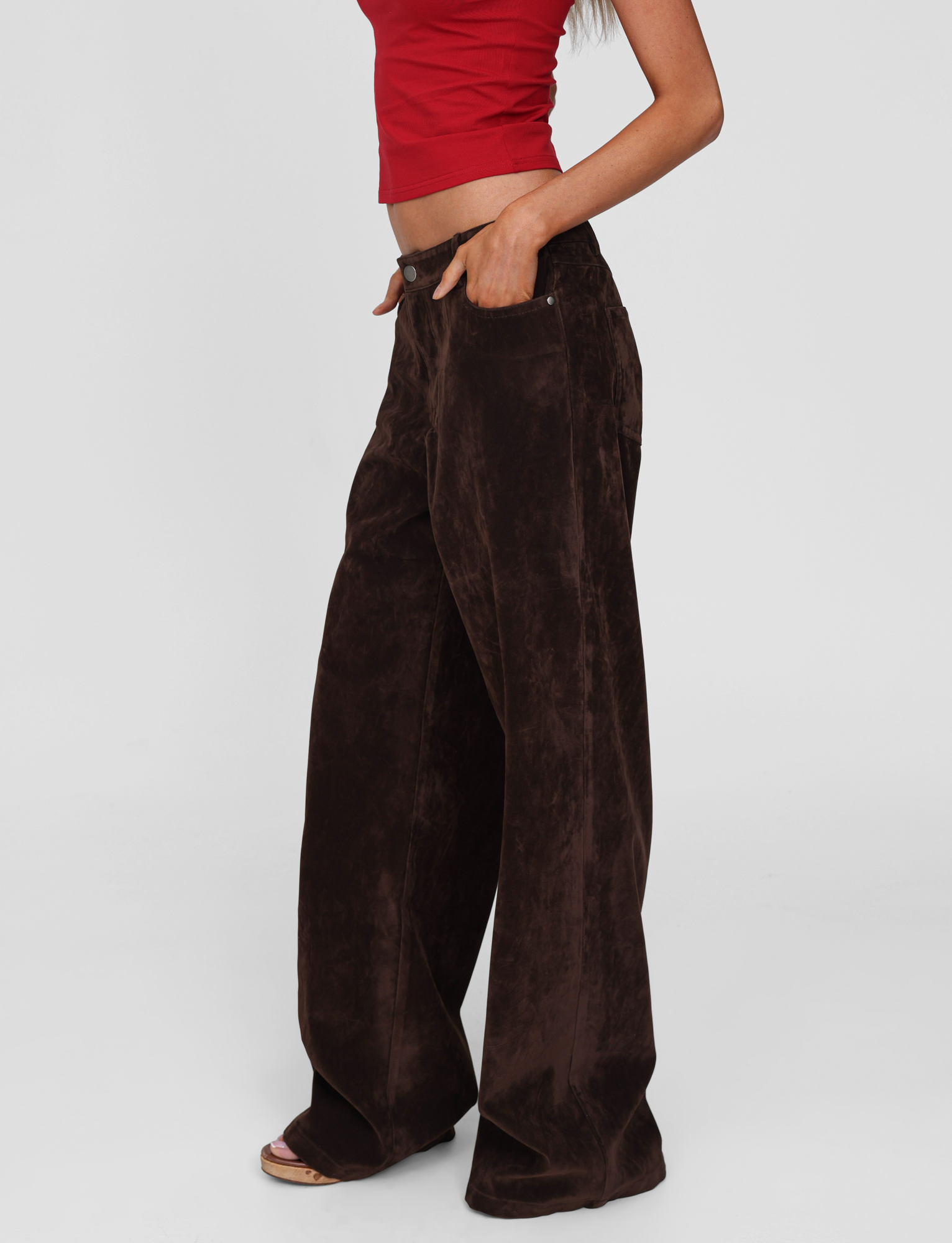 A person models the TIGERMIST CAMELLIA PANT in chocolate suede, featuring a high-waisted, straight-leg vintage design, paired with a red crop top against a plain white background.