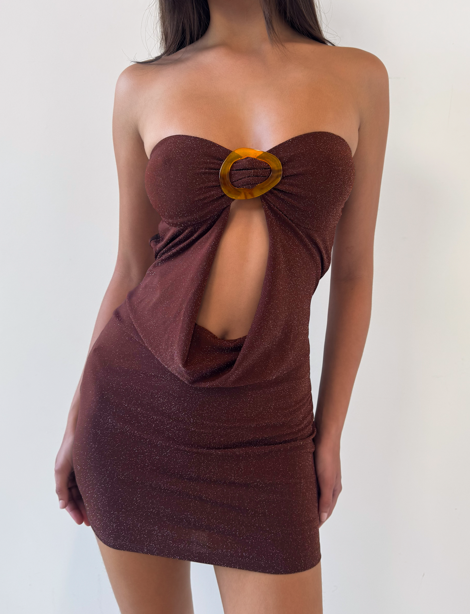 A woman wears the TIGERMIST KESTREL MINI DRESS in chocolate, featuring a strapless mesh design with a shimmery brown finish, front cutout, and large ring detail at the bust, standing against a plain white background.