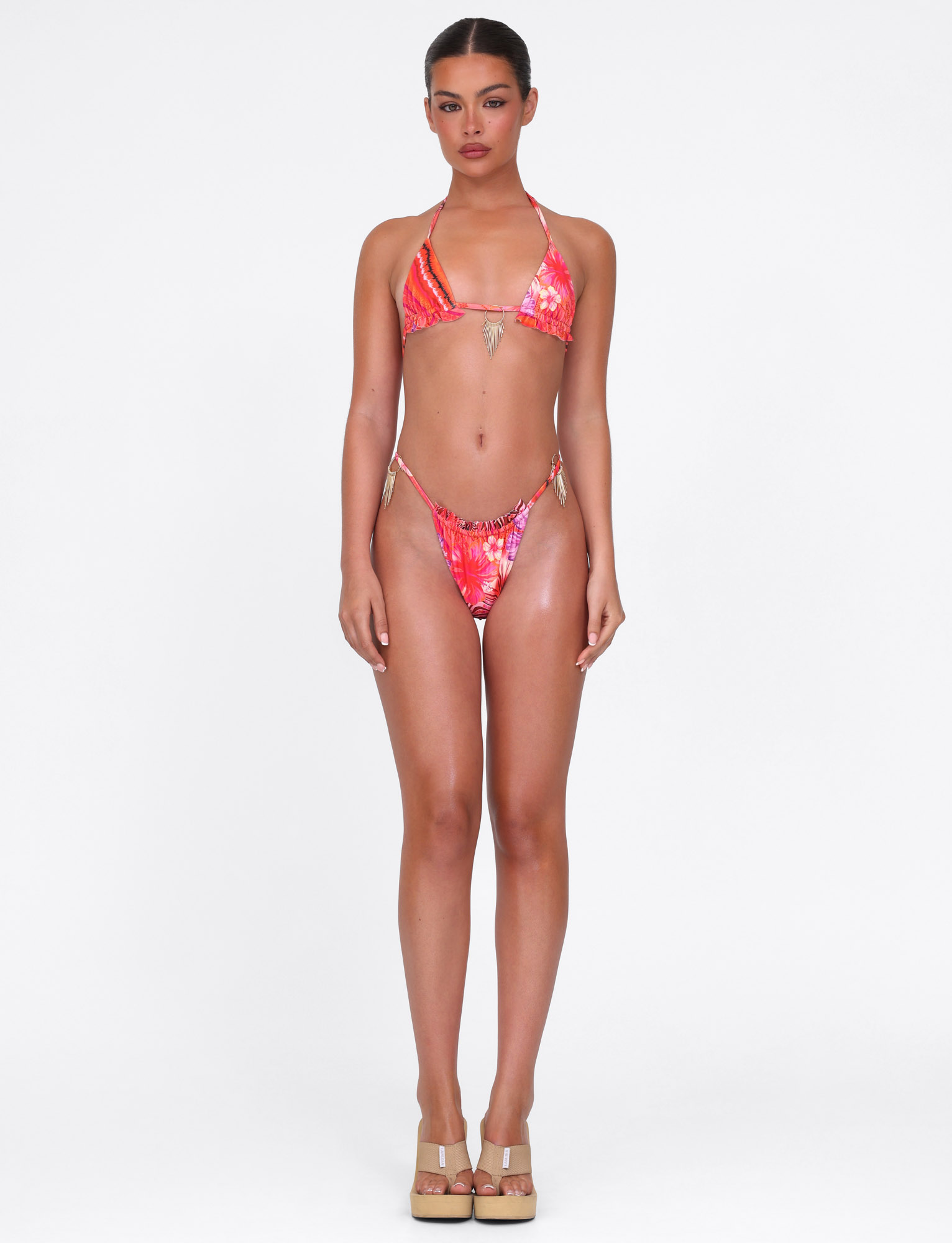 A woman stands against a white background wearing the TIGERMIST CIANA BIKINI TOP in Pink Tropical Floral, featuring an adjustable halter tie. She faces forward with a neutral expression and her arms relaxed at her sides.