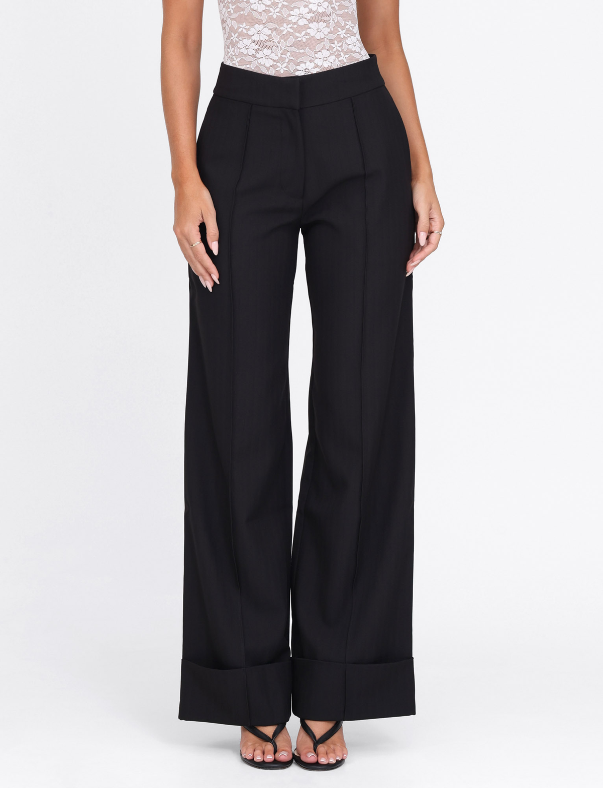 A person wears Tiger Mist’s BETHANY PANT - BLACK, styled with a white lace sleeveless top and black strappy heels, posing against a plain white background.