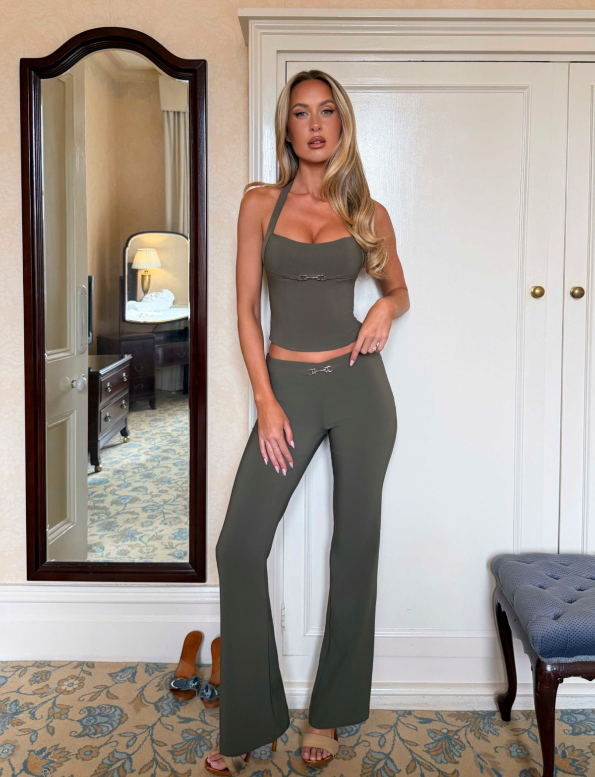 A woman wears a TIGERMIST KITTIE BUCKLE PANT - OLIVE in olive green, featuring a matching halter-neck top and pants with silver-toned buckle accents at the center.
