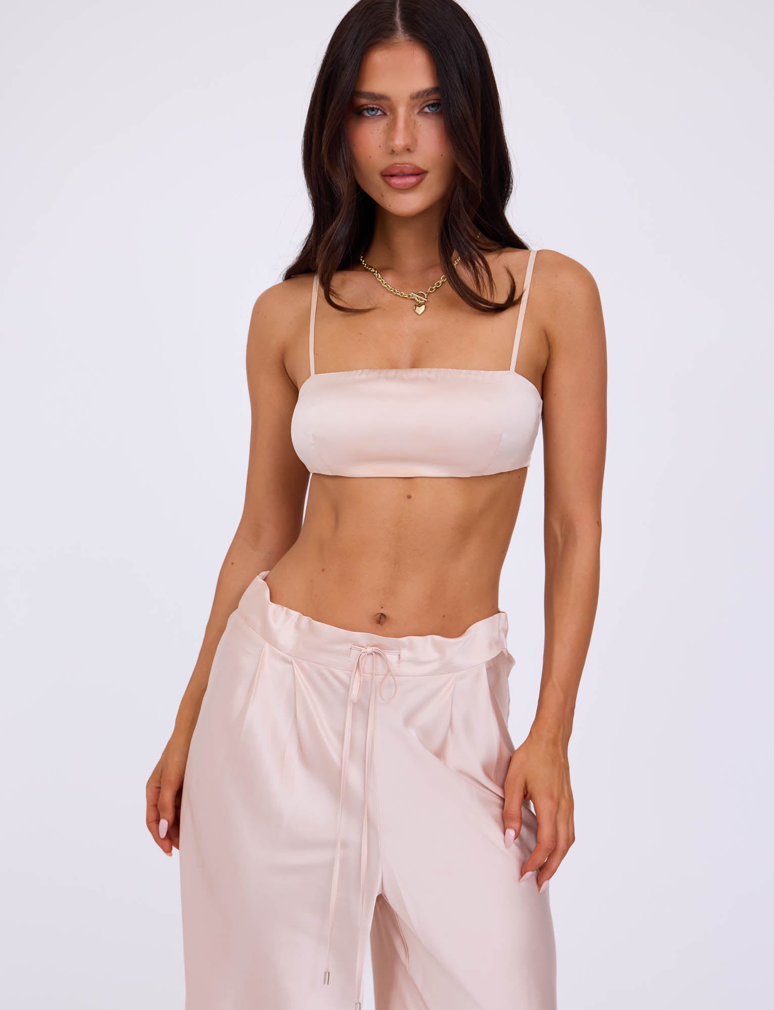 A person with long dark hair is modeling the Ivory ALINA Top from TIGERMIST, paired with matching loose-fitting Tiger Mist pants. The person stands against a plain white background, slightly tilting their head with a neutral expression and one hand resting on their hip.