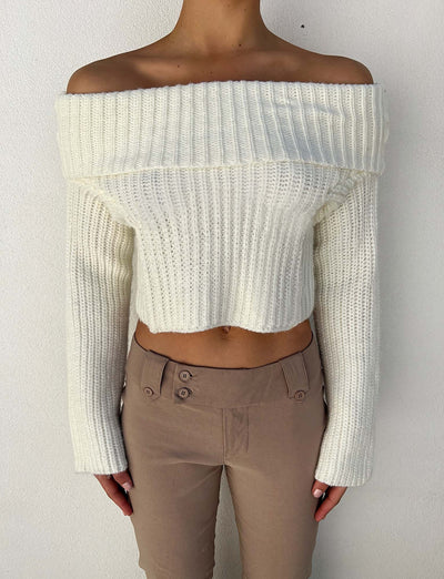 A person wearing the ASHLYN JUMPER in white from TIGERMIST and beige high-waisted pants with button details on the front. The background is a plain white wall.