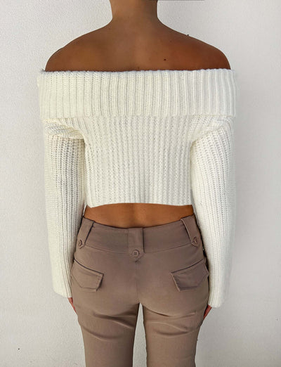 A person is seen from the back, wearing the Tigermist Ashlyn Jumper in white and beige pants. The off-the-shoulder white knit jumper features a ribbed texture that exposes the shoulders and upper back, while the beige pants include back pockets with button details. The background is plain white.