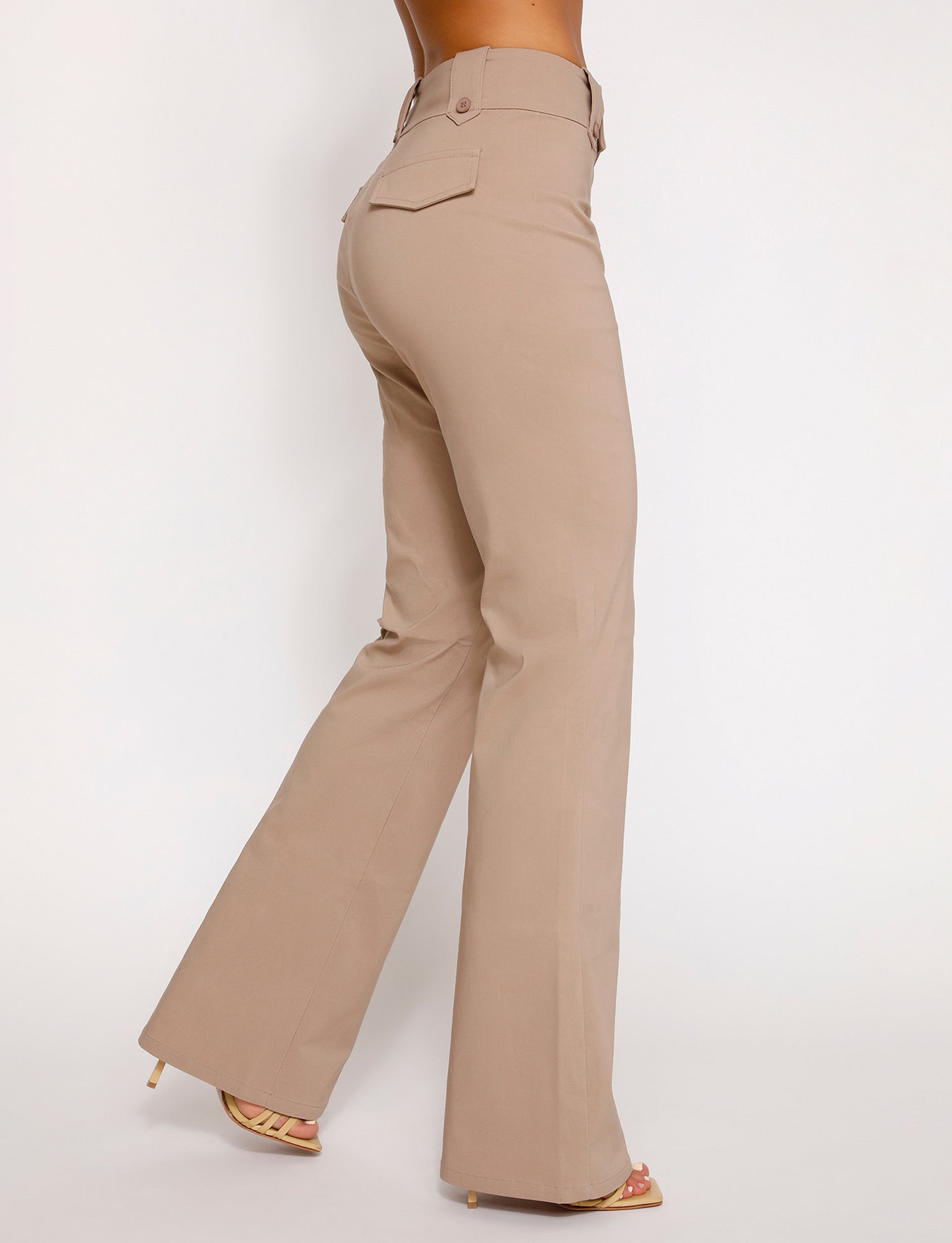 A person is modeling the KITTIE HIGH RISE PANT - BEIGE : TAN from the TIGERMIST collection, featuring a high-waisted, wide-leg design with flap pockets on the back. They are also wearing beige high-heeled sandals. The photo is taken from behind against a plain white background.