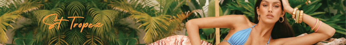 A woman in a blue bikini lounges on a patterned blanket surrounded by lush green tropical plants; "St. Tropez" is written in orange script on the left side.