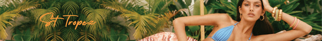 A woman in a blue bikini lounges on a patterned blanket surrounded by lush green tropical plants; "St. Tropez" is written in orange script on the left side.
