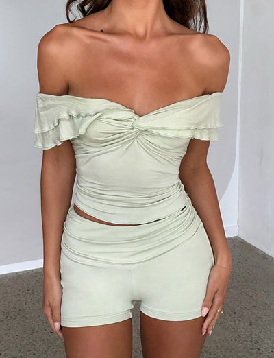 A woman is wearing the sage green DENALI TOP from TIGERMIST along with matching high-waisted shorts. She stands against a plain background with her hands by her sides, and her head is cropped out of the frame.