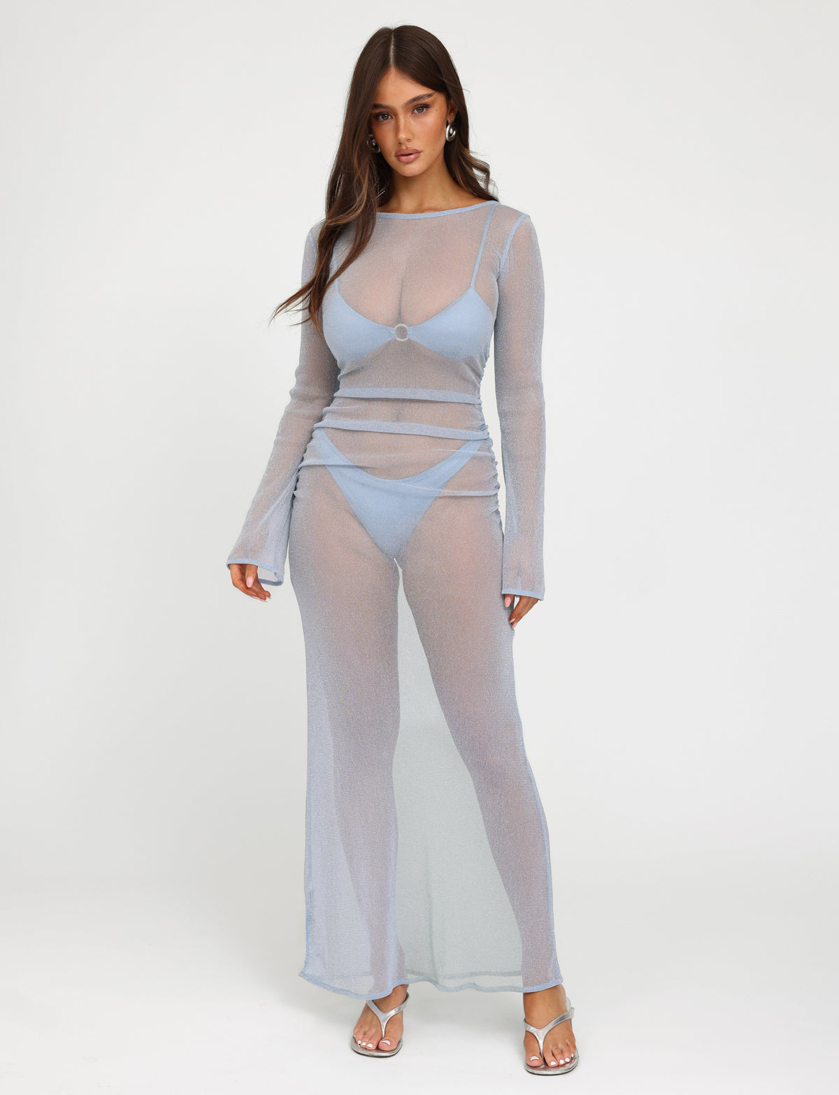 A woman is wearing the Alayna Three Piece Maxi Dress in pale blue from Tigermist. She has long, loose hair and stands against a plain white background, completing her chic look with heeled sandals.