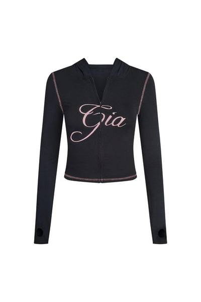 The BLARE HOODIE by I.AM.GIA is a black, long-sleeve, zip-up cropped hoodie with pink stitching, thumb holes, and "Gia" in bold pink cursive across the chest—ideal for a signature bodycon look.