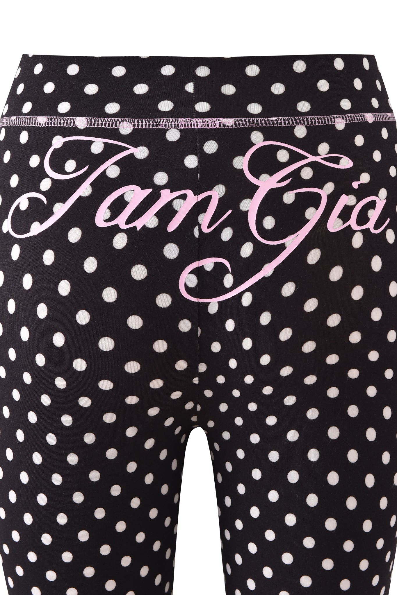Close-up of BLARE TRACKPANT - BLACK POLKA DOT by I.AM.GIA, featuring black leggings with white polka dots and pink cursive "I.AM.GIA" text across the back.