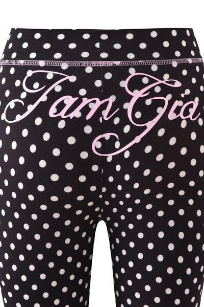 Close-up of BLARE TRACKPANT - BLACK POLKA DOT by I.AM.GIA, featuring black leggings with white polka dots and pink cursive "I.AM.GIA" text across the back.