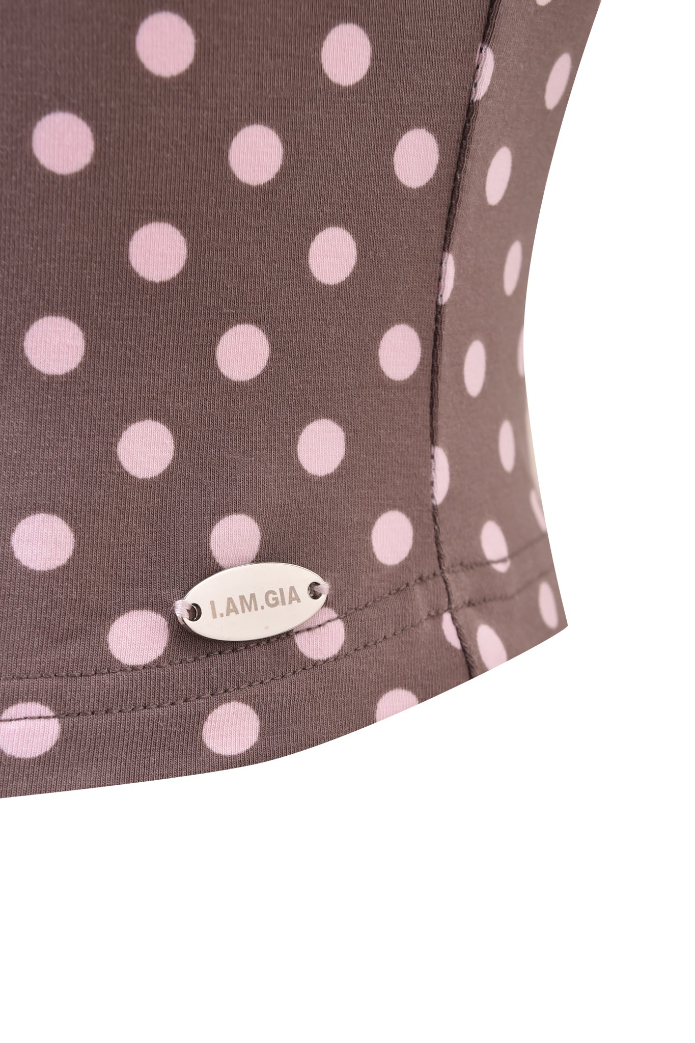 Close-up of the BLARE HALTER STRAP TOP - PINK CHOCOLATE by I.AM.GIA, showing brown fabric with light pink polka dots and a small metallic "I.AM.GIA" tag sewn near the hem.