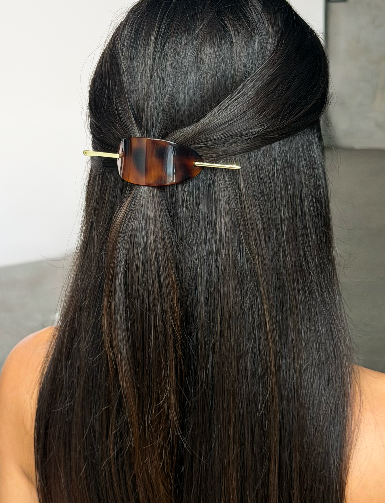 A person with long, straight, dark hair styled half-up and secured from behind with the TIGERMIST RUKA BARRETTE in tortoiseshell.