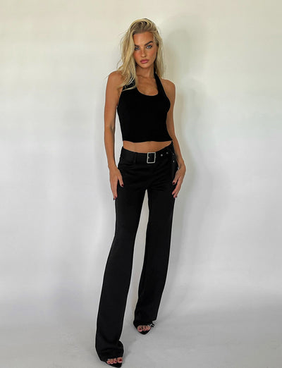 A person with long blonde hair stands confidently against a plain background, wearing a black sleeveless top and the HADLEY PANT - BLACK from TIGERMIST. They pose with one hand resting on their hip and the other lightly touching the side of their pants.