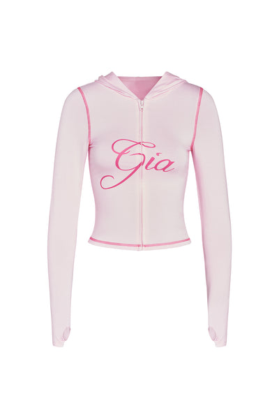 The I.AM.GIA BLARE HOODIE in pastel pink is a cropped zip-up with long sleeves, thumb holes, and "Gia" in bold, cursive dark pink on the front for standout style.
