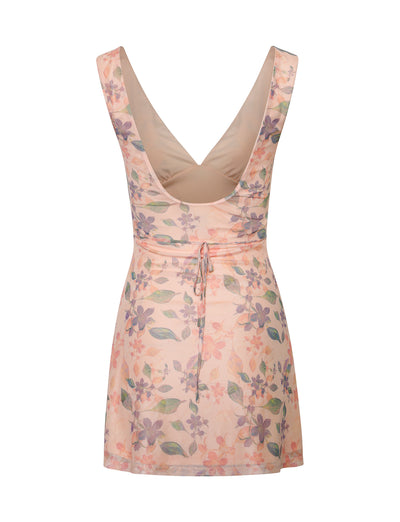 The TIGERMIST CYRUS DRESS in ORANGE : PEACH WATERCOLOUR FLORAL is a sleeveless dress featuring a deep V back and a floral pattern with vibrant pink, purple, and green hues on a light beige background. It includes an adjustable waist string and has a mid-thigh length hemline.